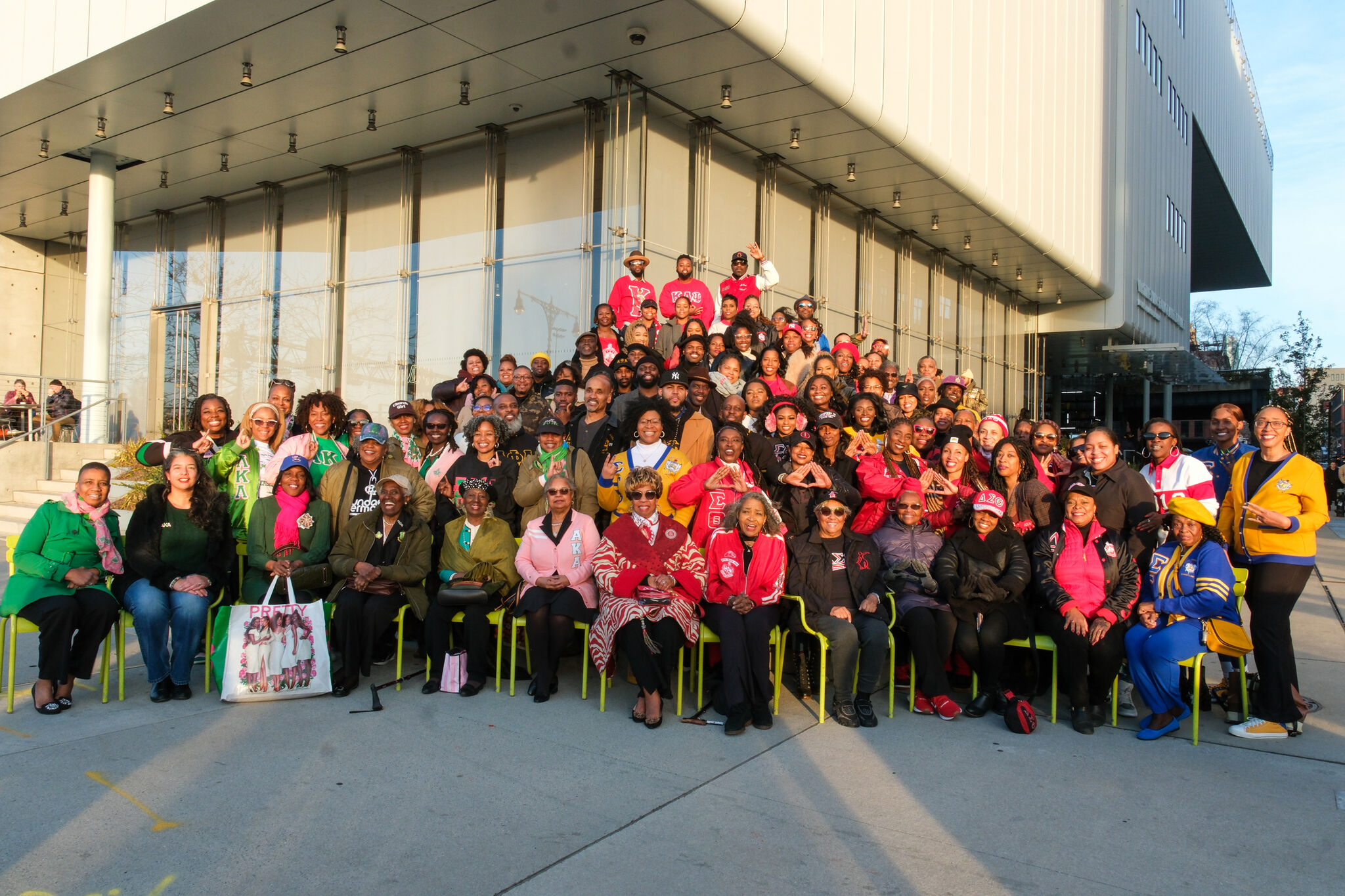 A large group of people wearing colorful organization jackets pose together outside the Whitney Museum of American Art.