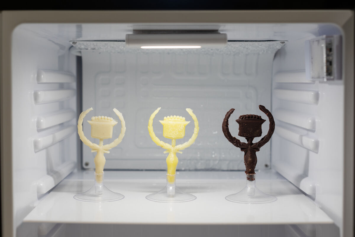 Three figures made of chocolate, butter, and plastic sit poised in a refrigerated container.