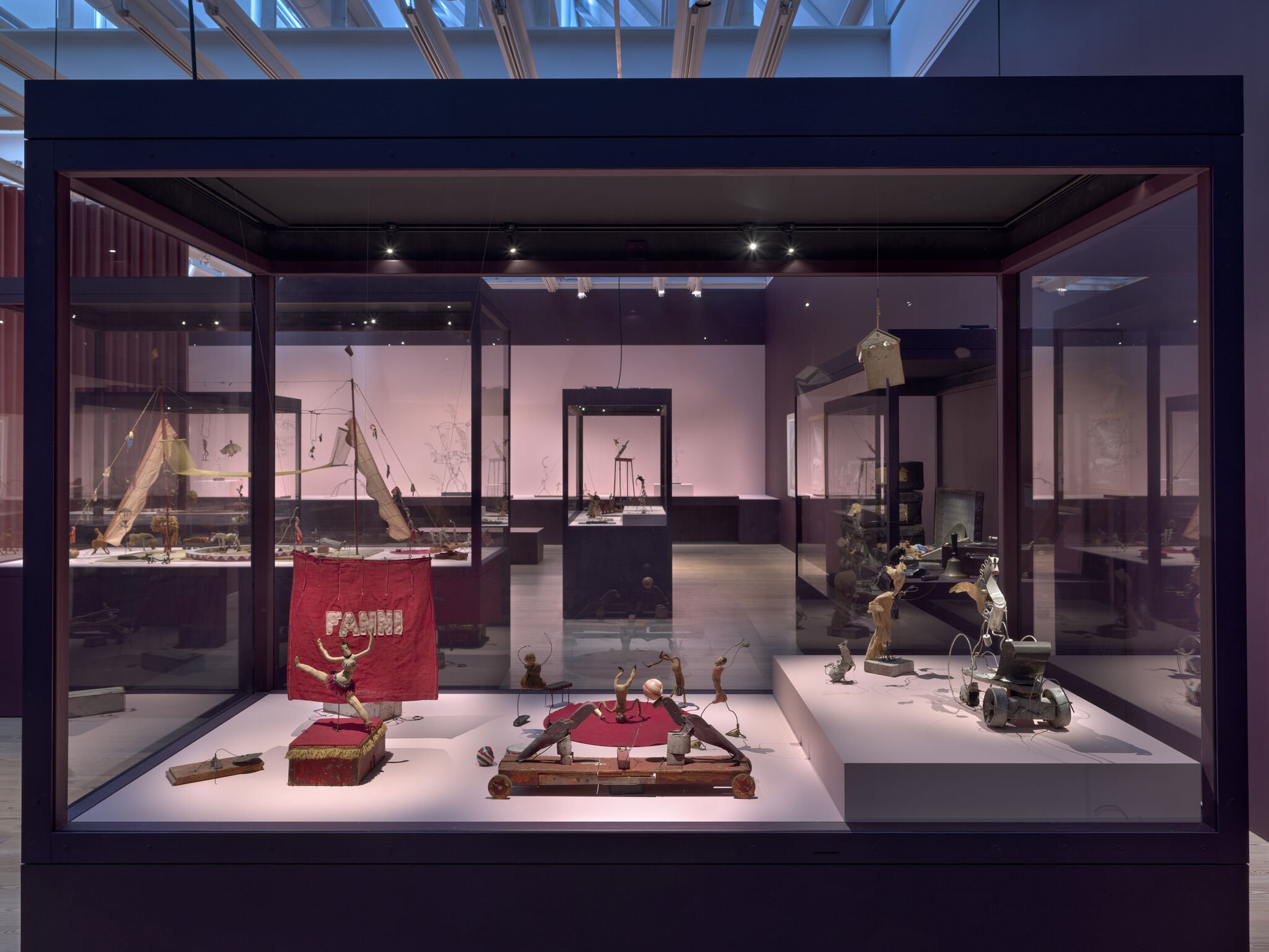 A glass display case holds vintage mechanical toys and puppets arranged on platforms under museum lighting.