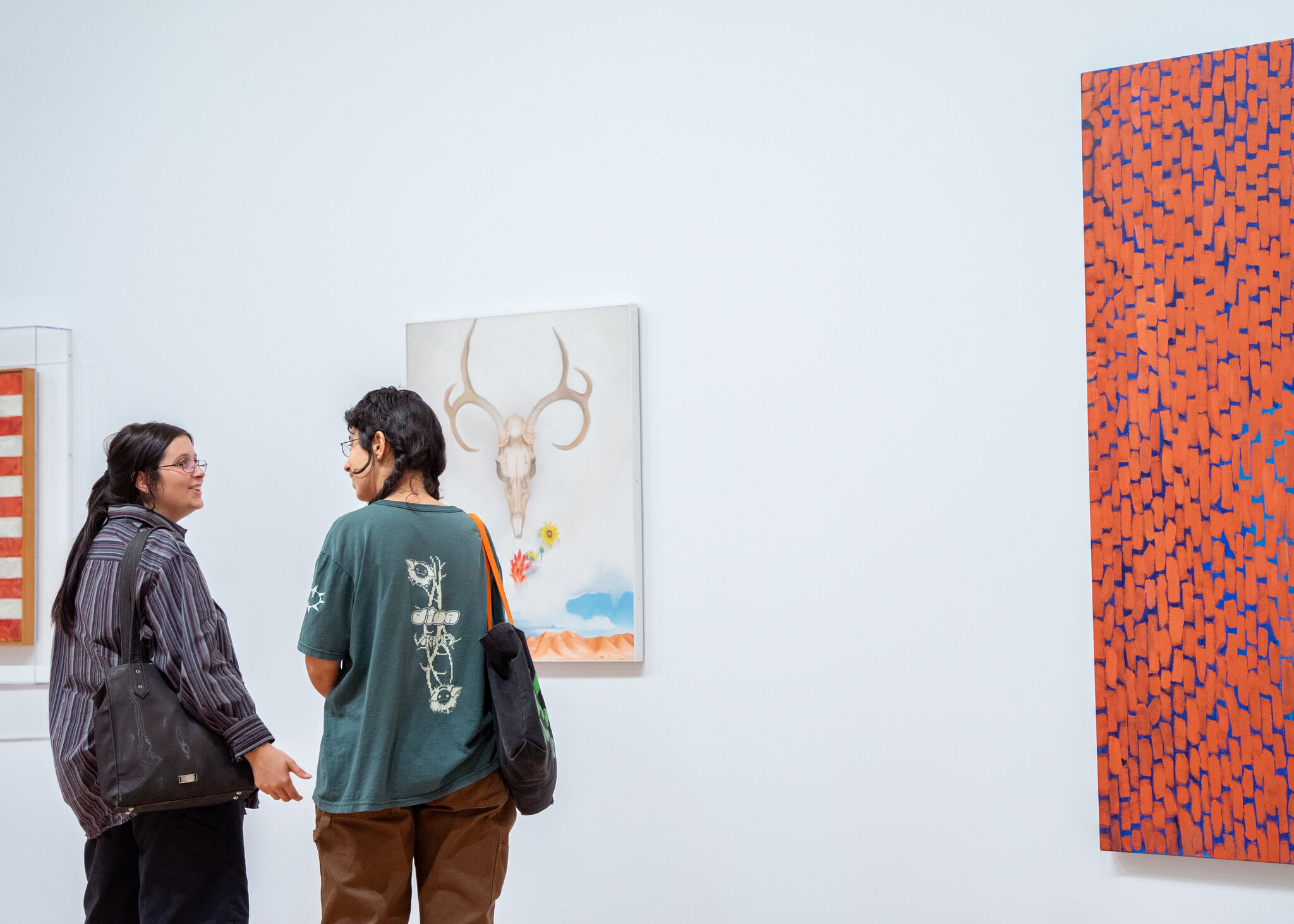 Two people talk while looking at a skull-themed painting in a bright art gallery.