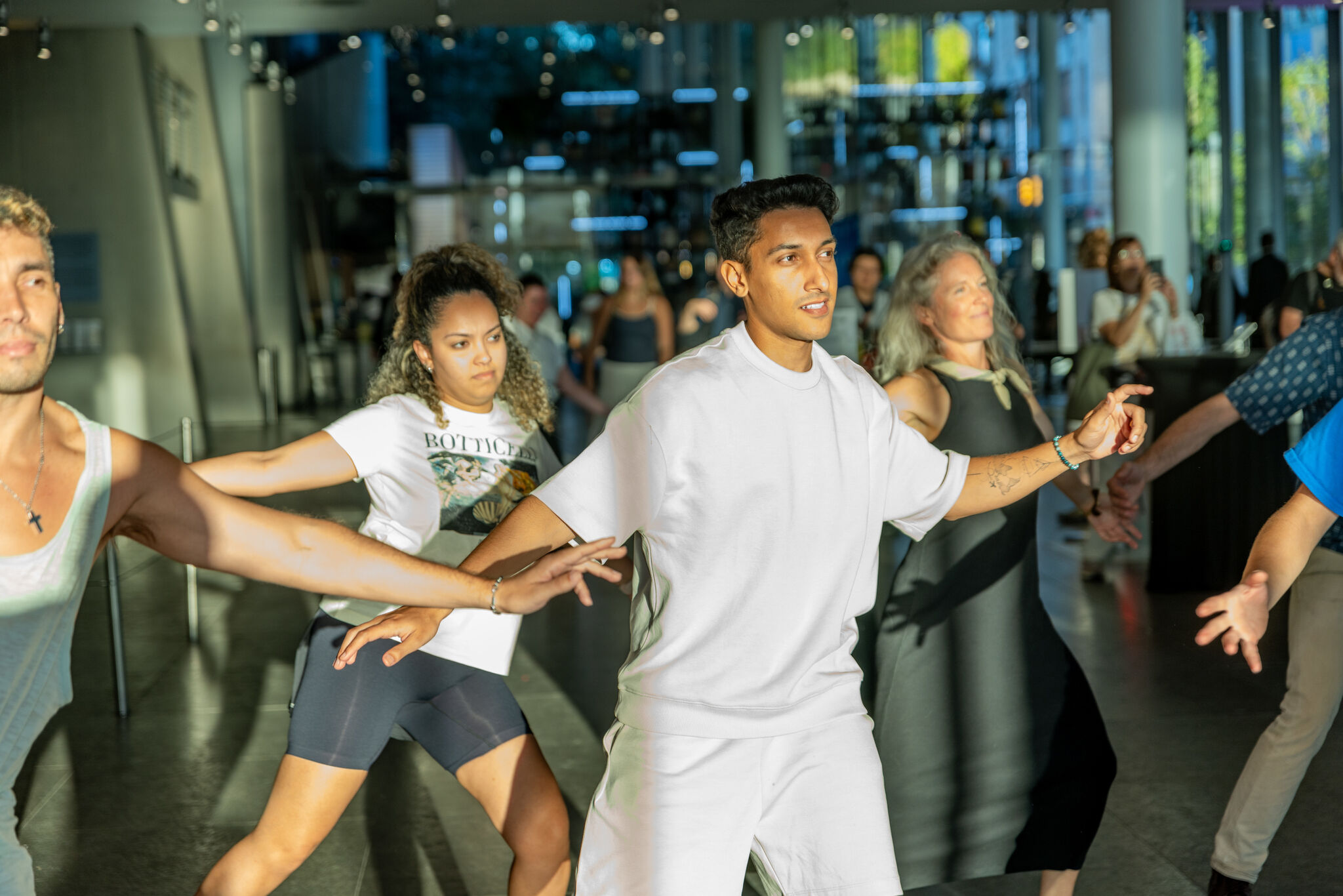 A young man leads a diverse group practicing a dance routine with outstretched arms.