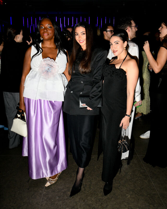 Three women pose together at a nighttime event, dressed in formal evening gowns and smiling.