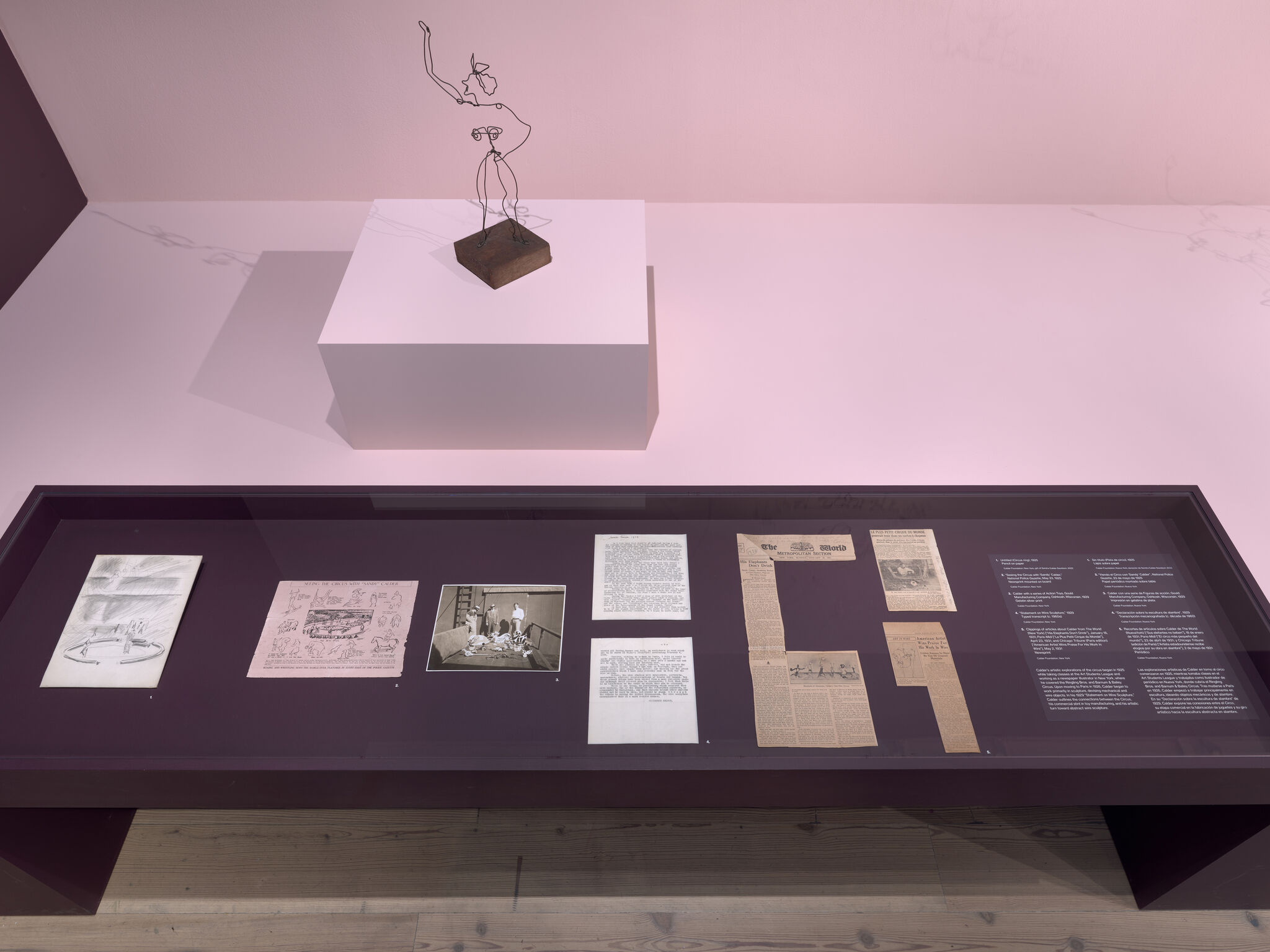 Small wire figure sculpture on a pedestal with a display case of historical documents beneath.