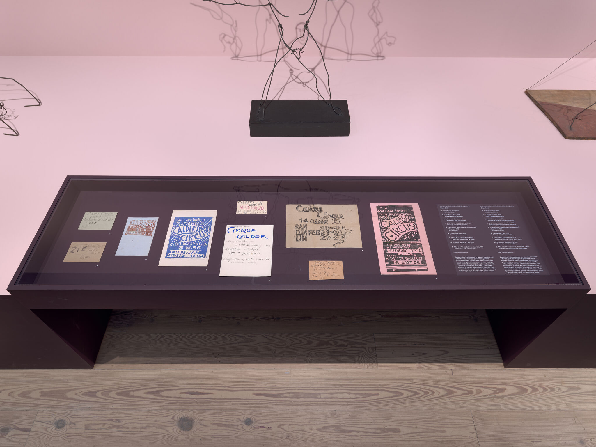 Display case showing vintage Calder Circus posters and handwritten notes on a pink gallery floor.