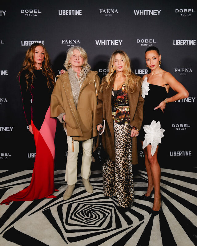 Four women pose together on a patterned floor in front of a Whitney event backdrop.