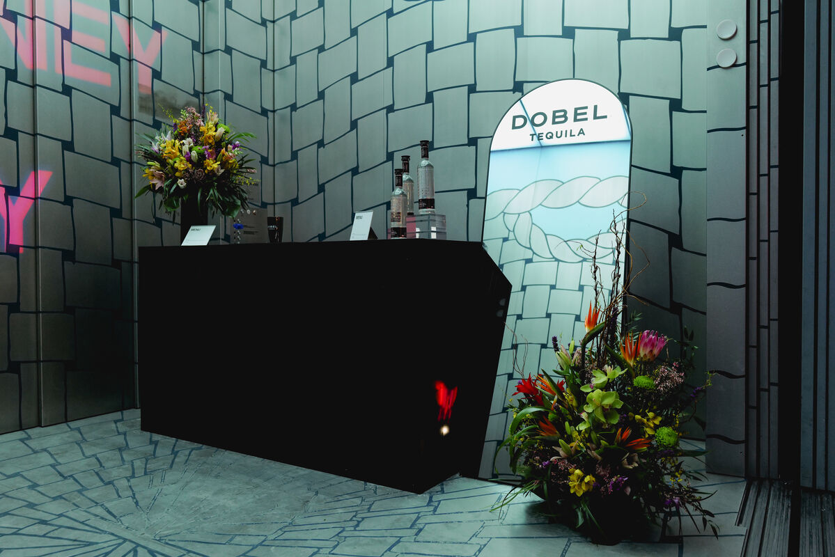 A black reception counter with tequila bottles and flower arrangements beside a Dobel Tequila display.