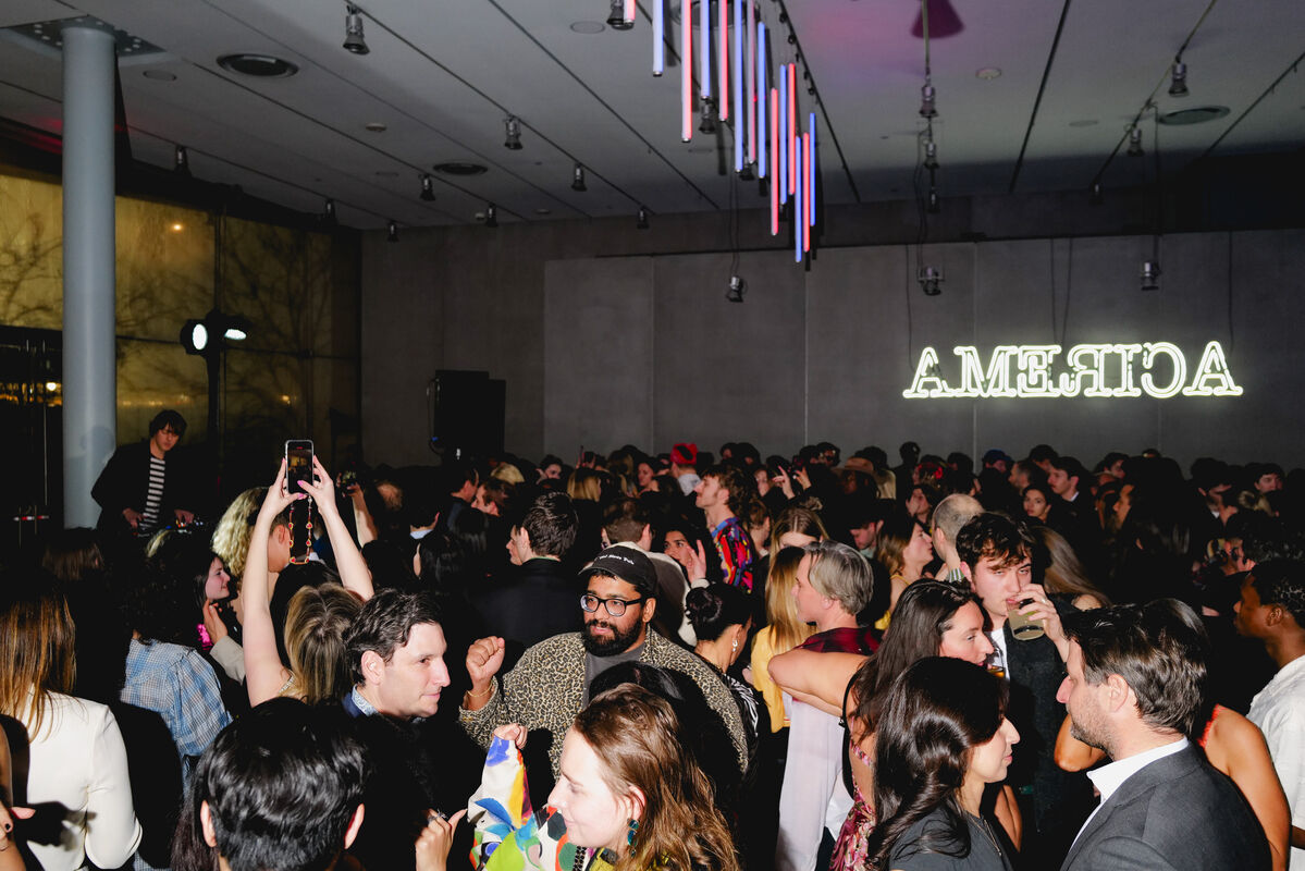Crowded indoor party with people dancing, talking, and taking photos under colorful lights.