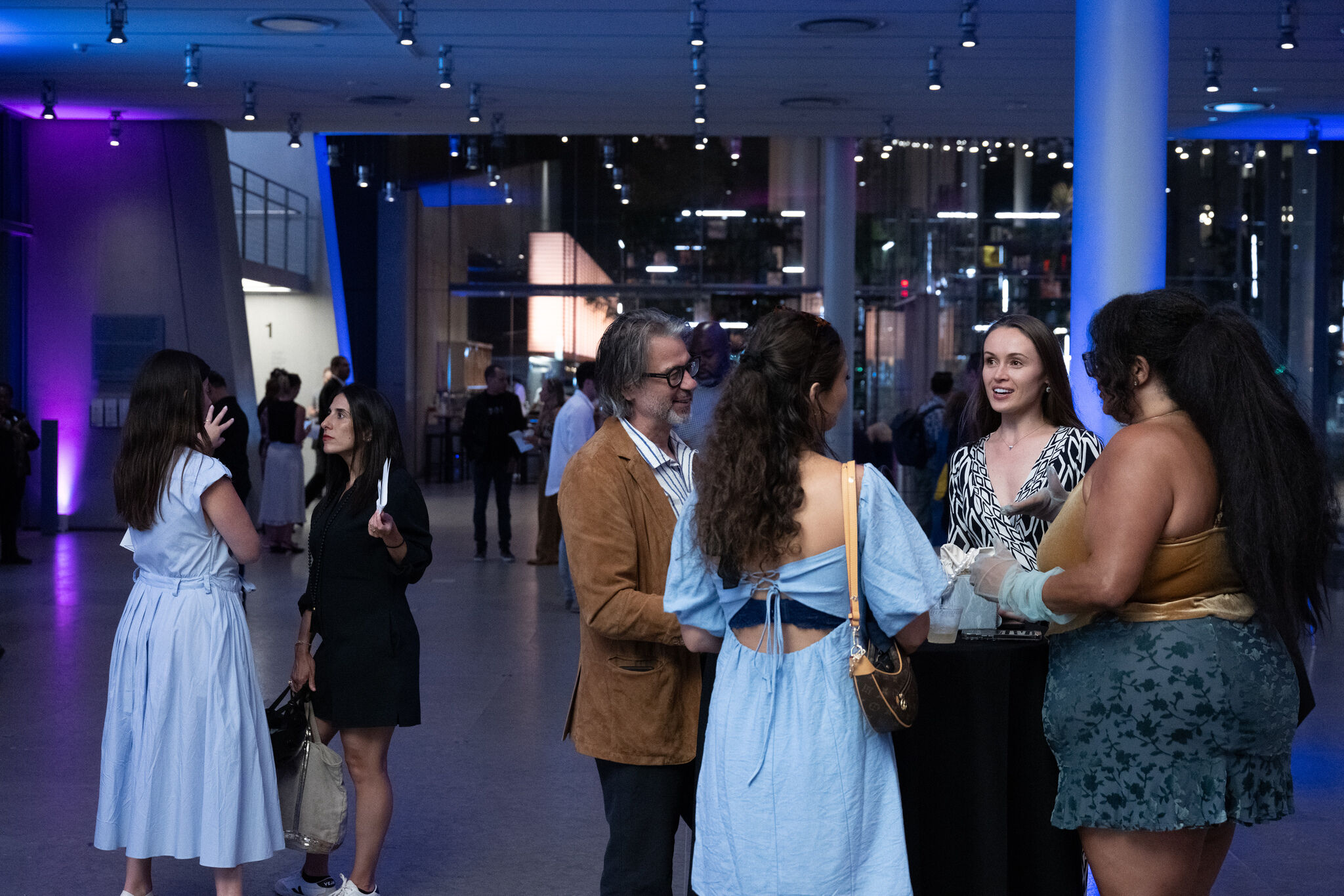 A group of people stand and chat around a high table in a modern blue-lit lobby.