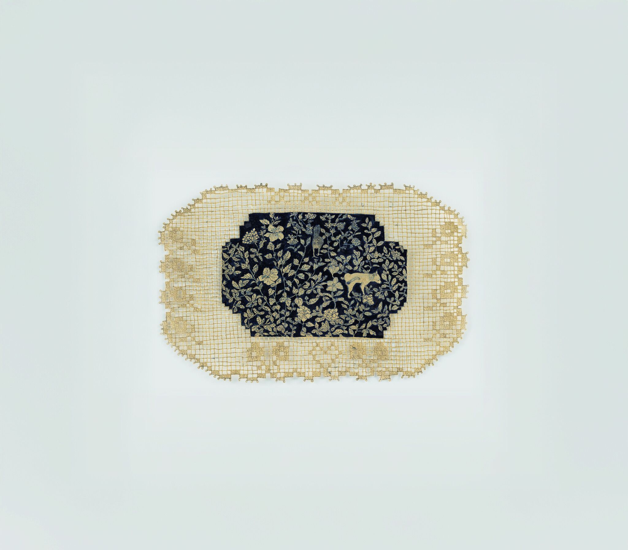 Rectangular lace doily with dark embroidered center showing floral pattern and a small animal figure.