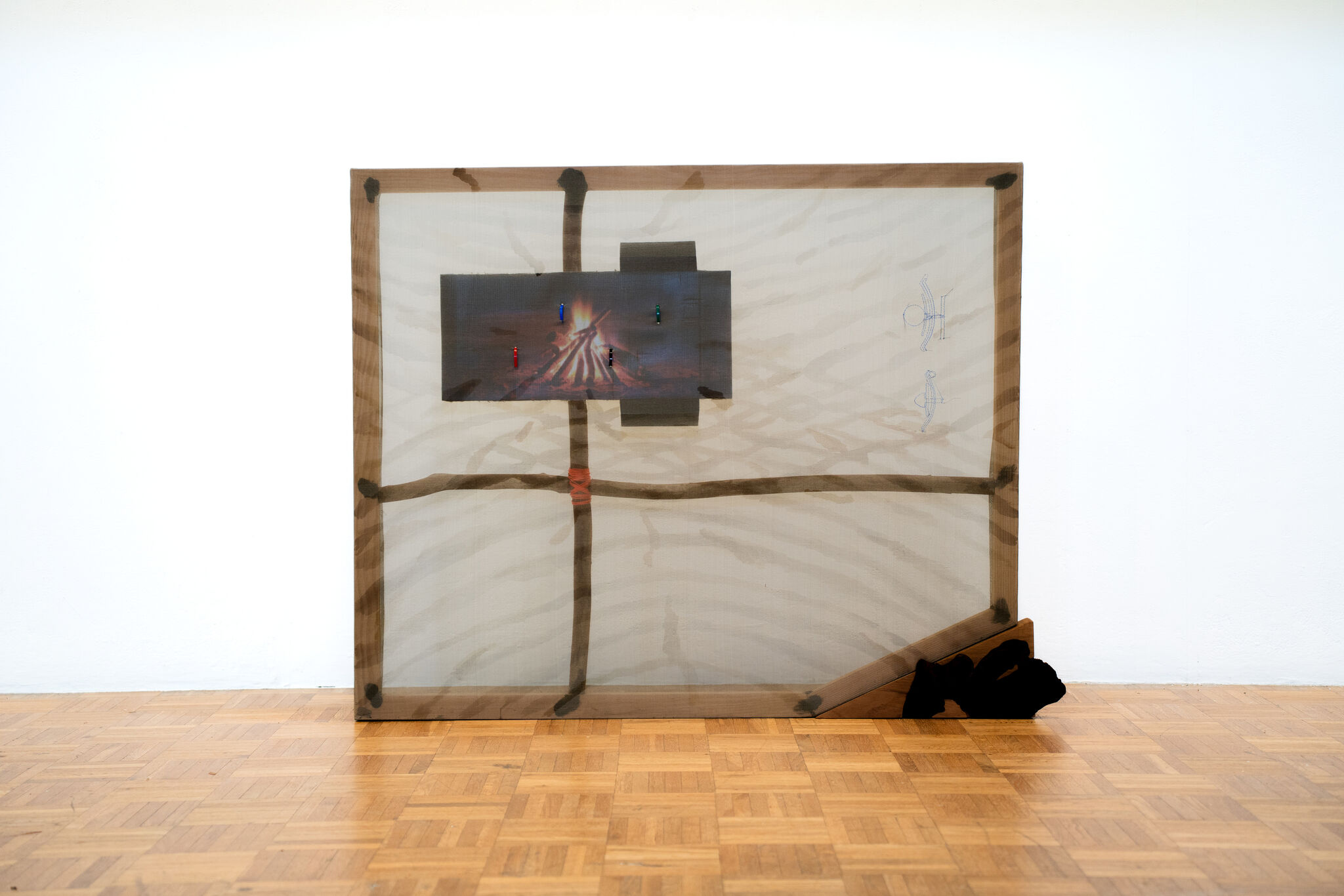 A large translucent fabric frame leans against a wall with a small lit campfire image attached.
