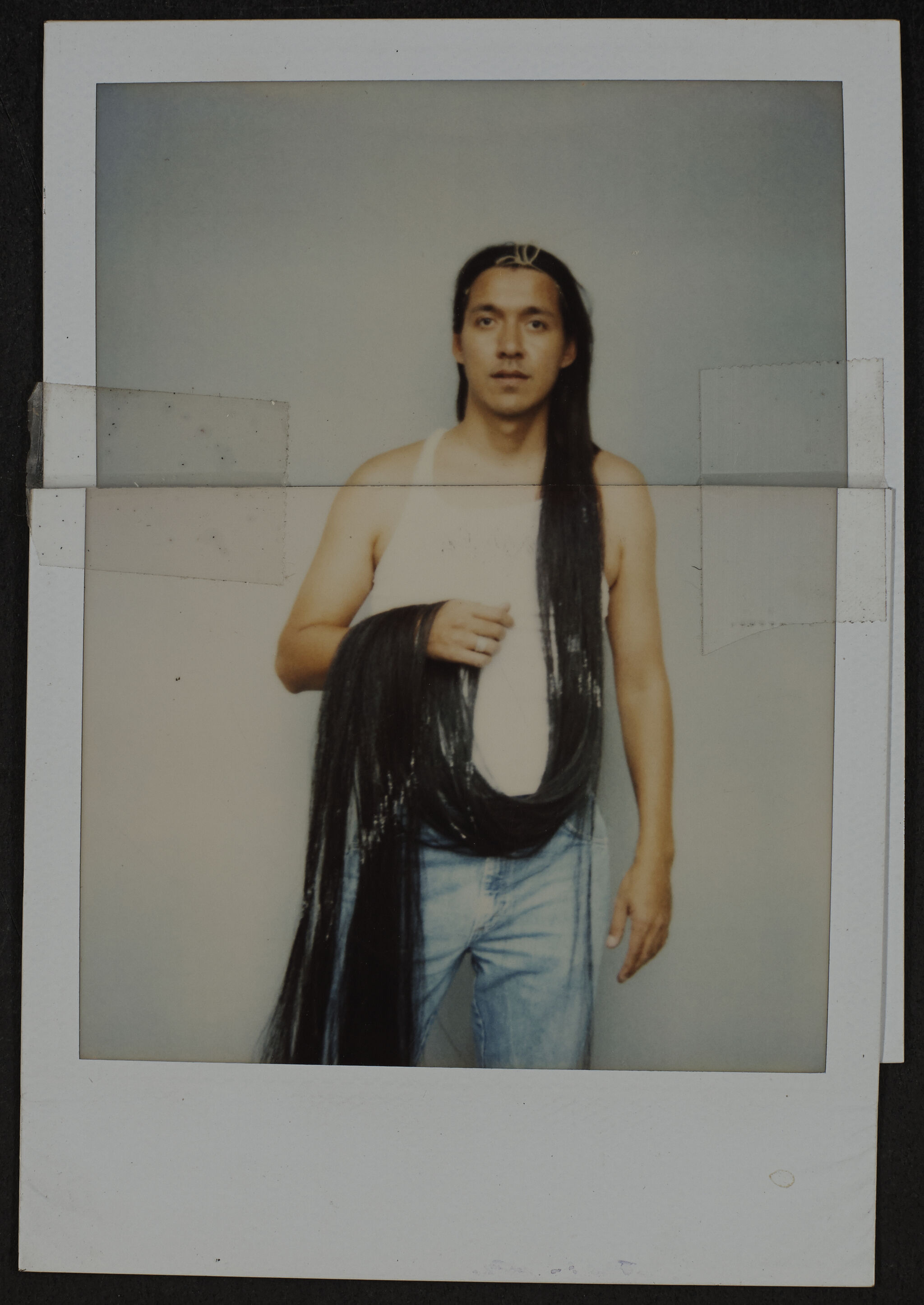 A man stands holding a long loop of dark hair draped around his torso and hand.