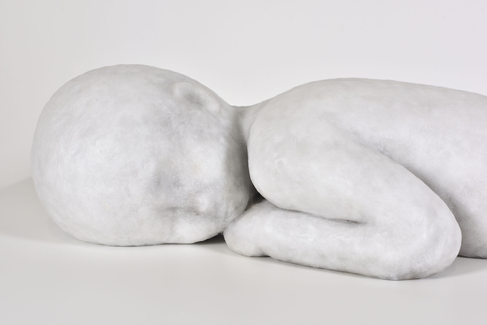 A smooth white sculpture of a curled sleeping infant lying on its side with arms tucked.