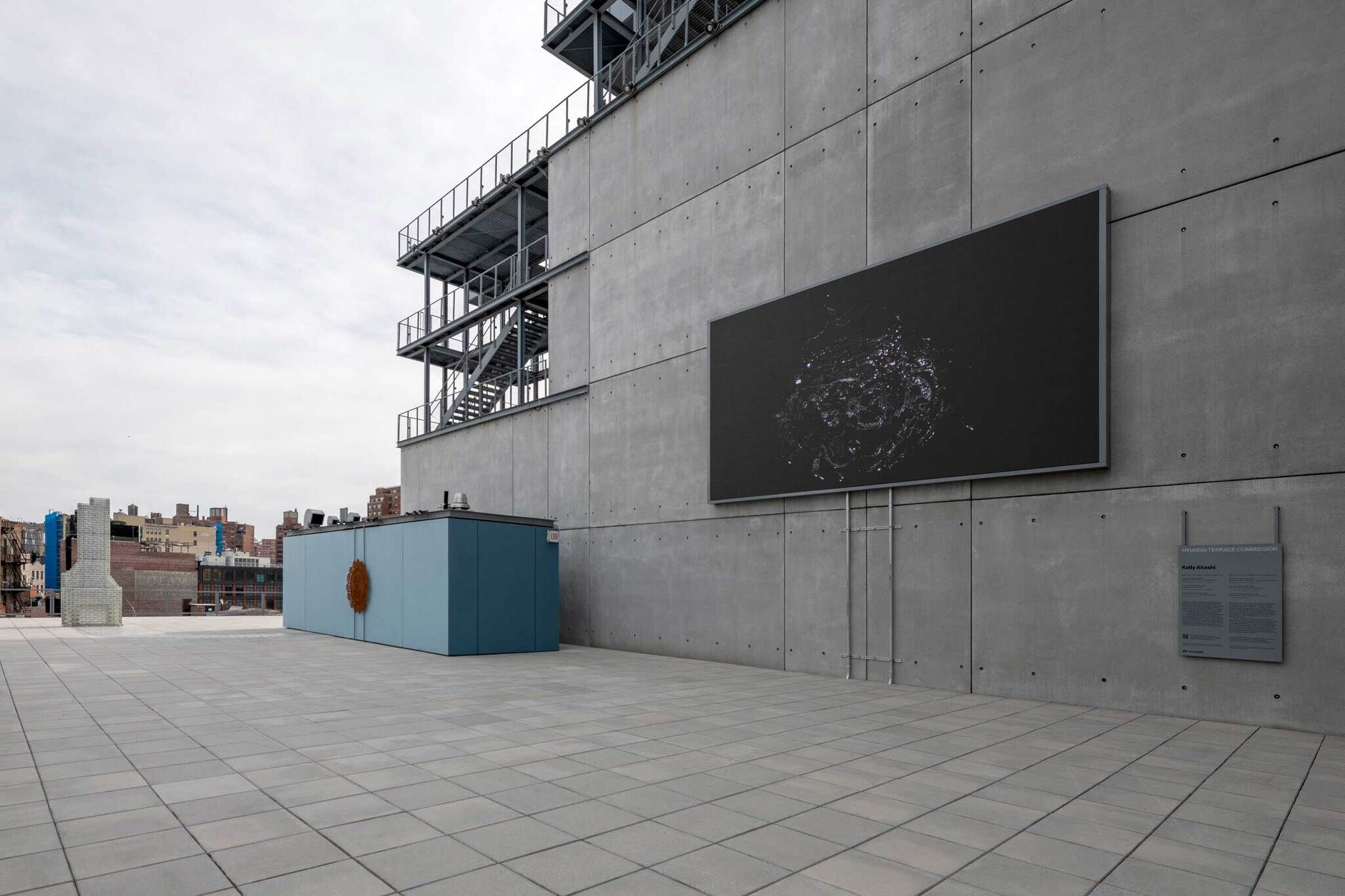 Large black digital screen mounted on a concrete building wall above an empty rooftop plaza.