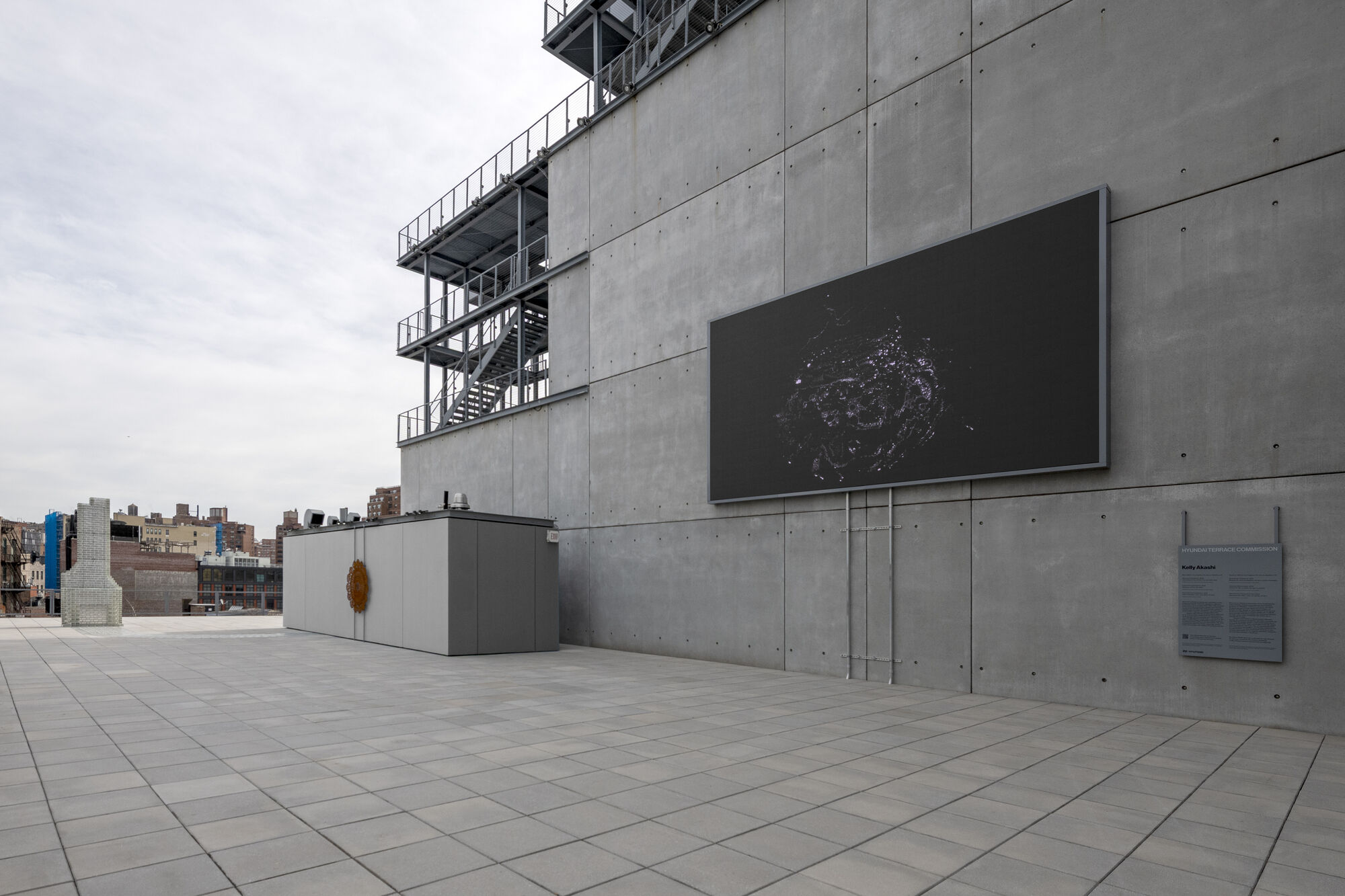 Large dark digital screen mounted on concrete building wall above empty tiled rooftop terrace.