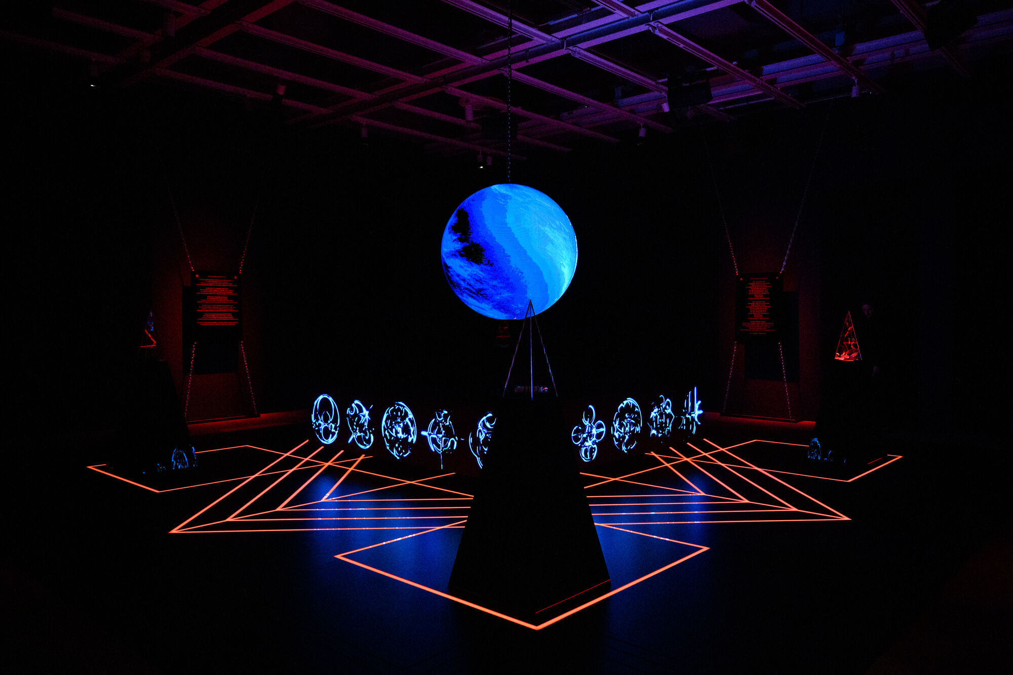 A glowing blue planet hangs above a ring of illuminated symbols with red geometric floor lines.
