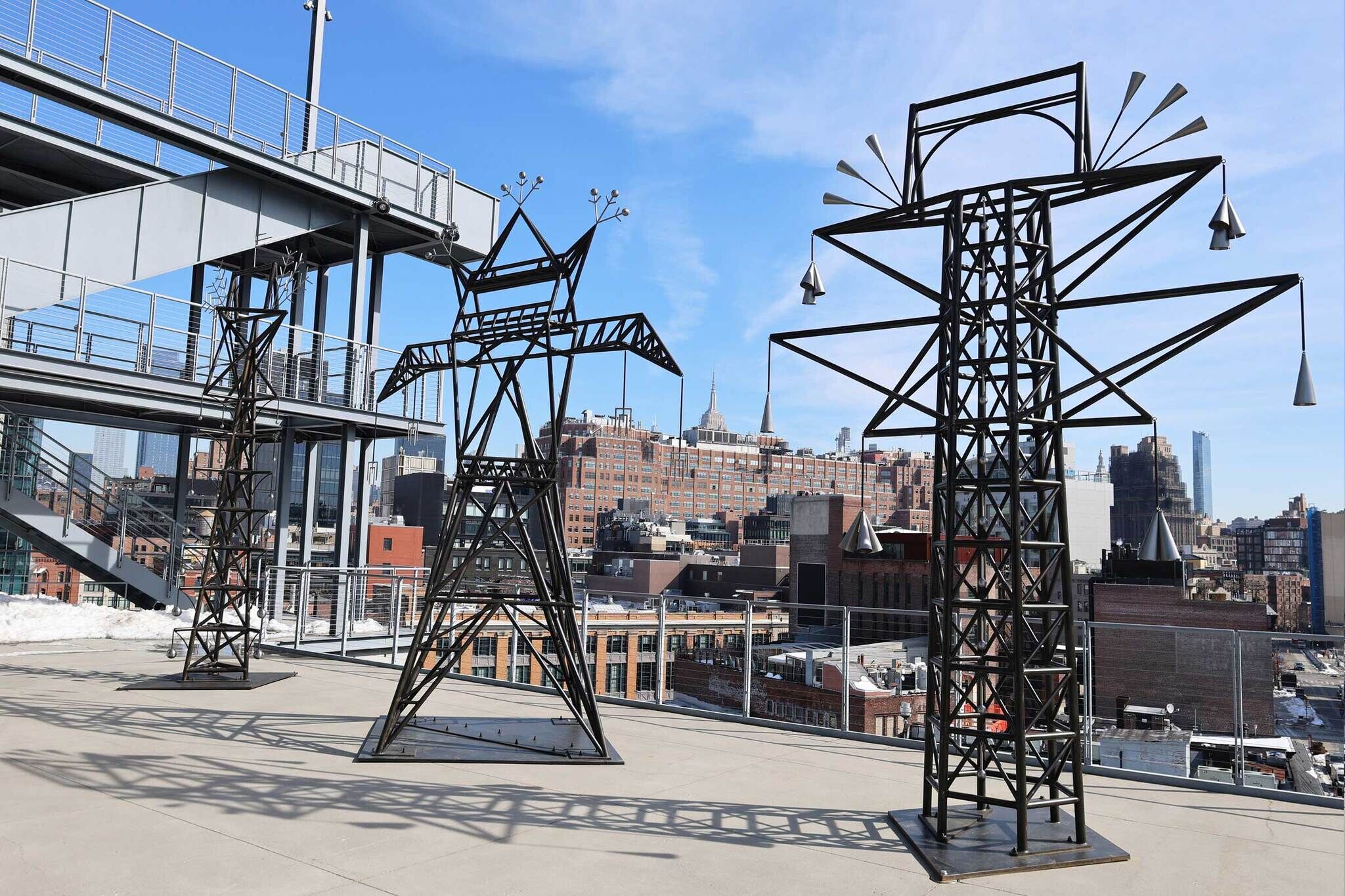 Three tall metal sculpture towers stand on a rooftop overlooking a city skyline.