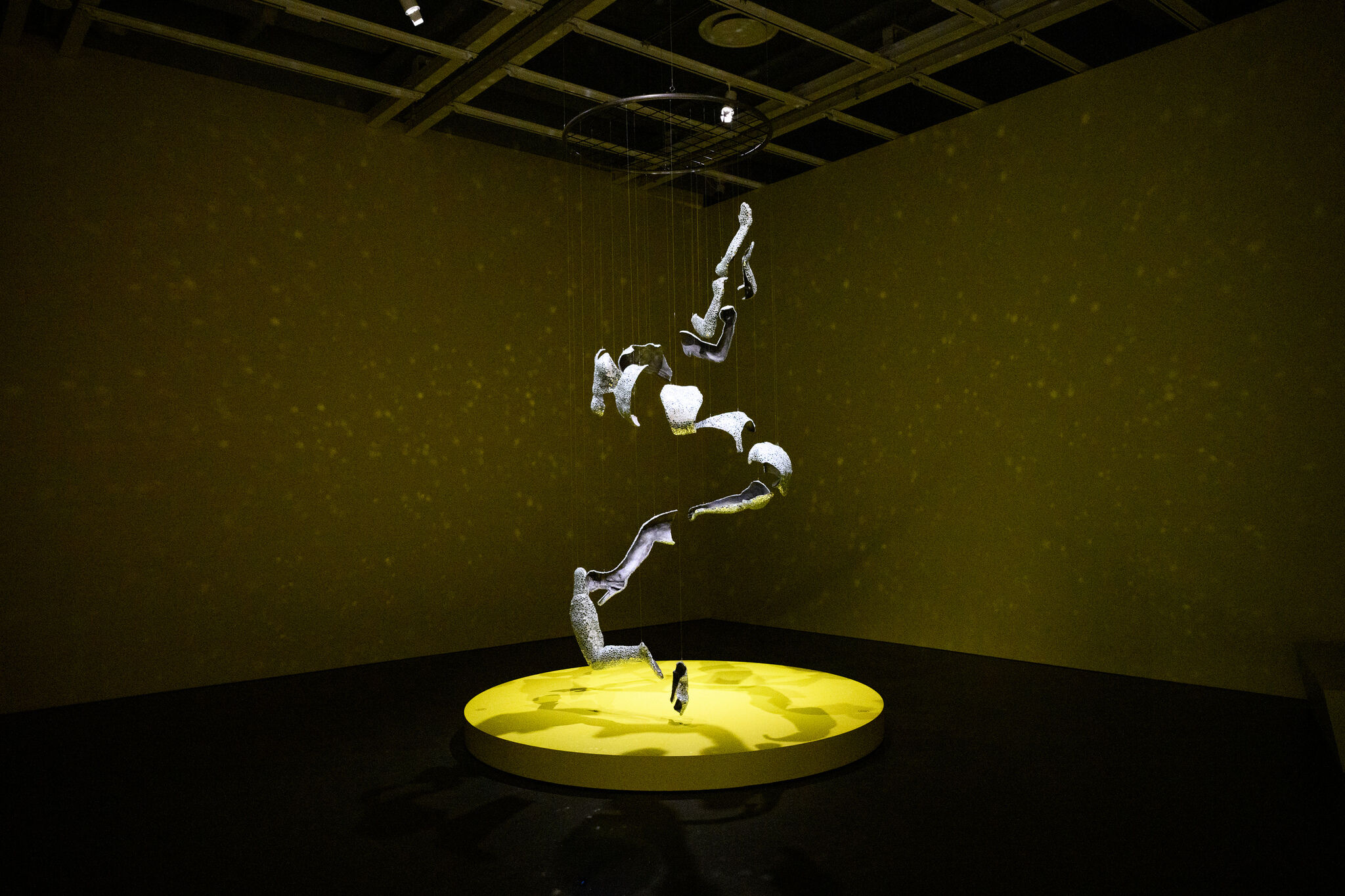 Suspended spiral of white fragmented sculptures hangs above a glowing yellow circular platform.