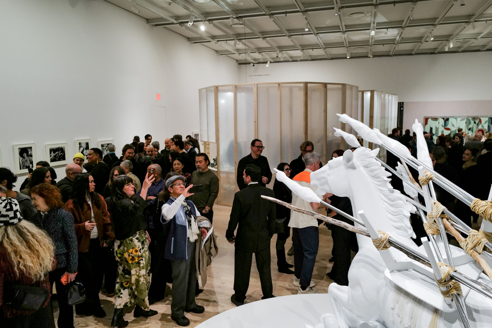Crowded gallery of visitors photographing and viewing a large white horse sculpture with bundled arrows.