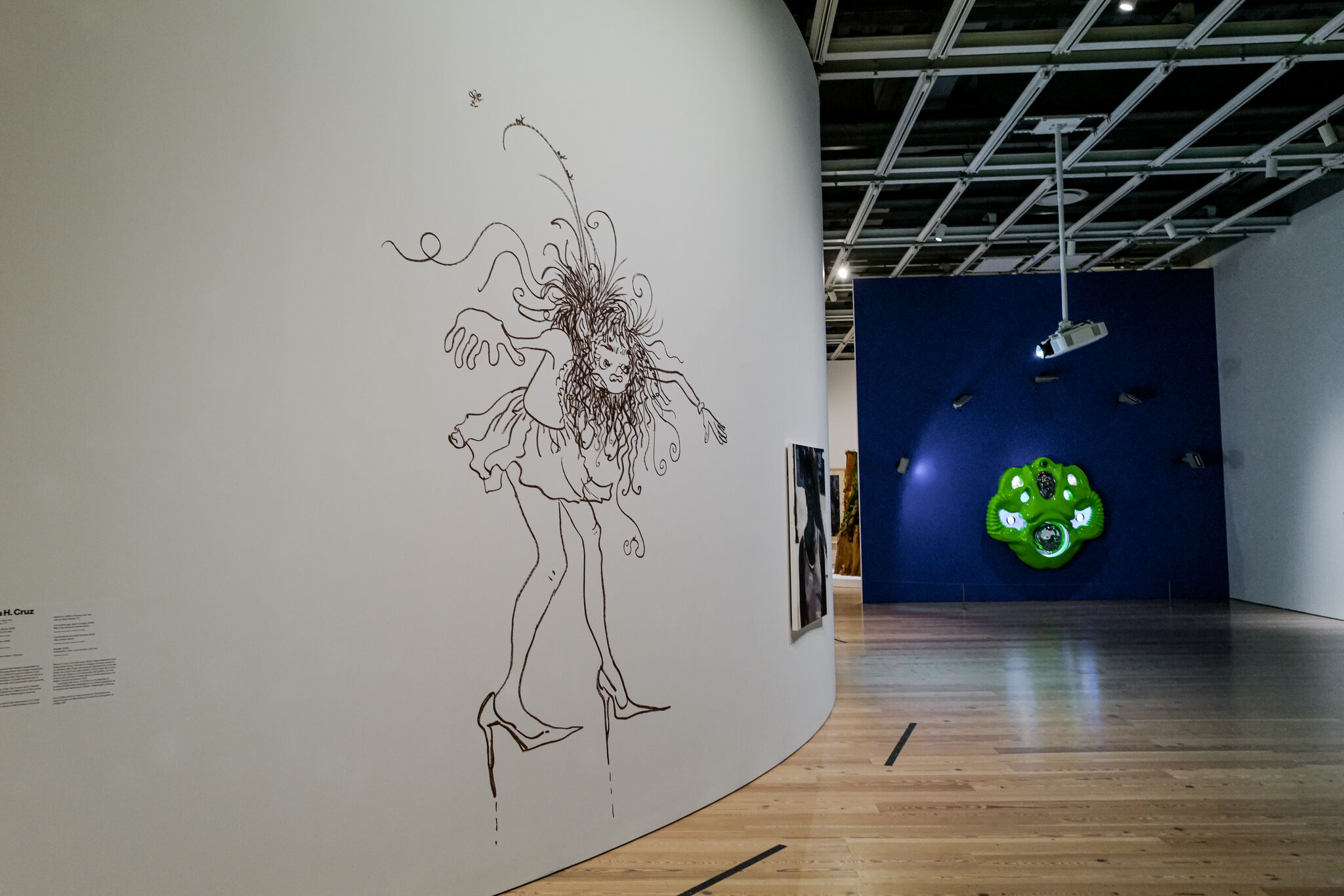 Large black line drawing of a hunched woman in a dress and high heels on a curved gallery wall.