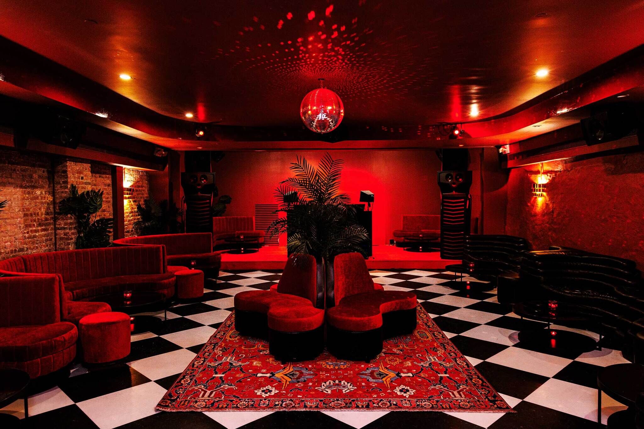A red-lit lounge with black-and-white checkered floor, central circular seating, and a disco ball.