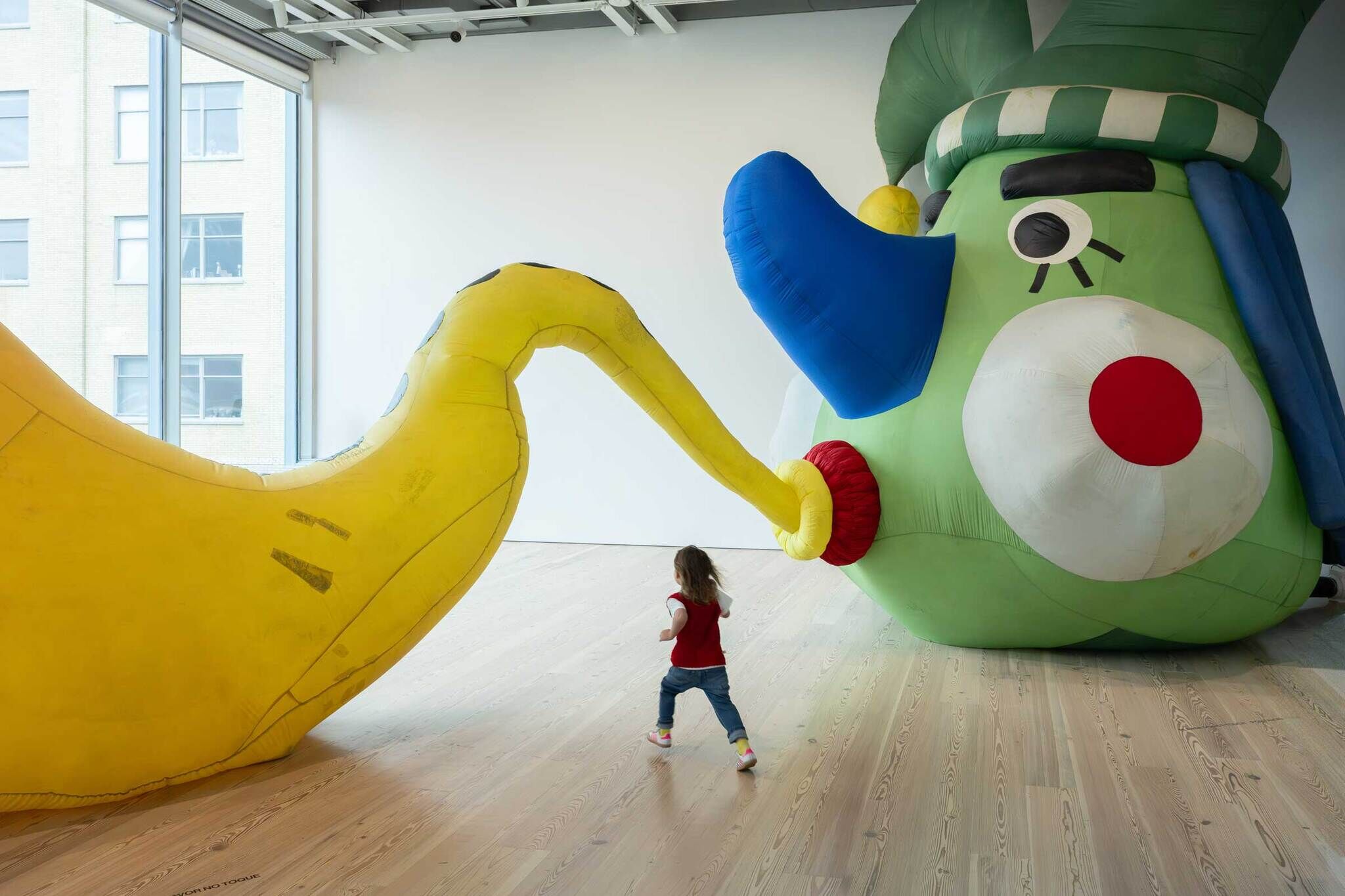 A young child runs toward a giant colorful inflatable sculpture with a long yellow tube.