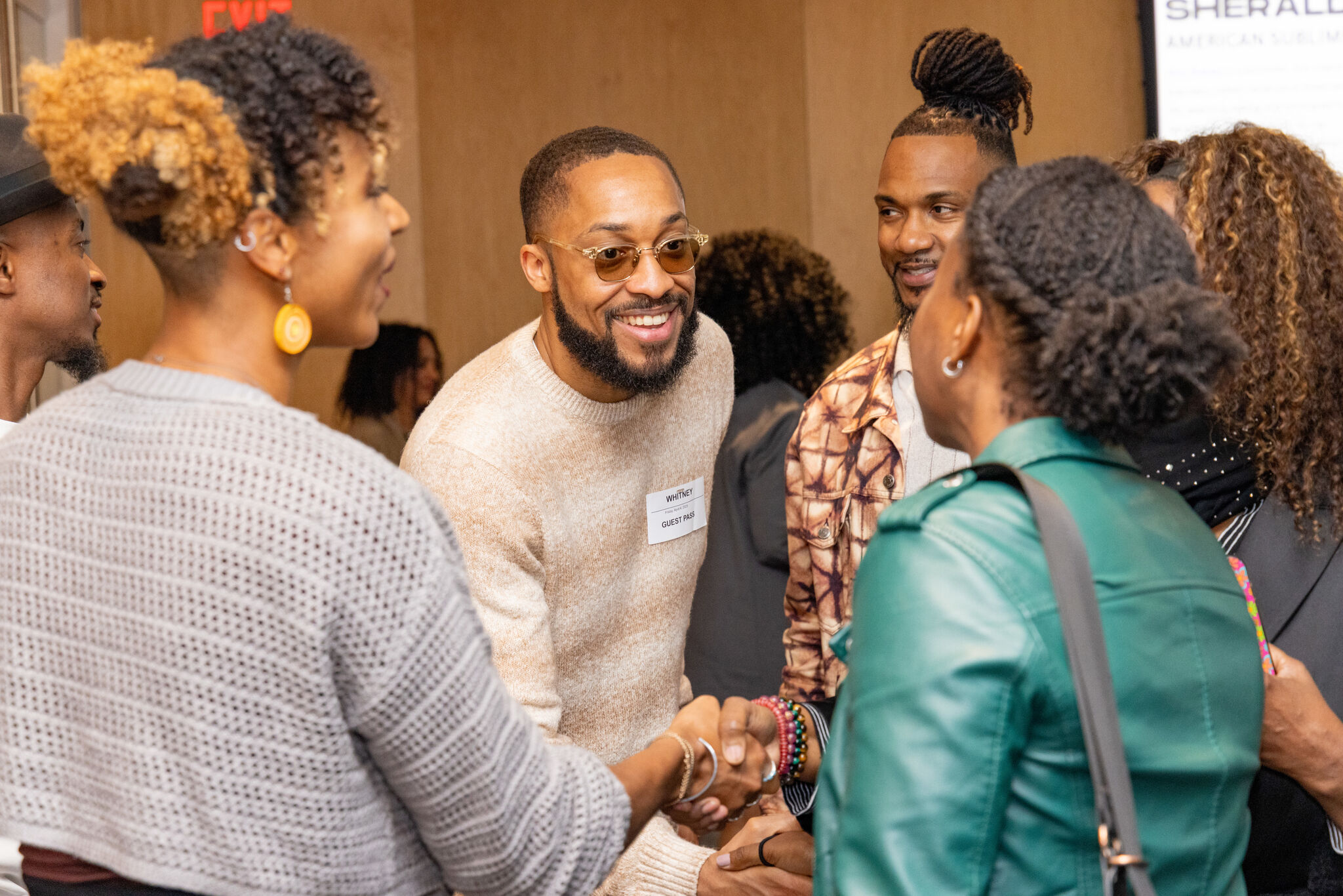 A smiling man with glasses warmly shakes hands while talking with a small group.