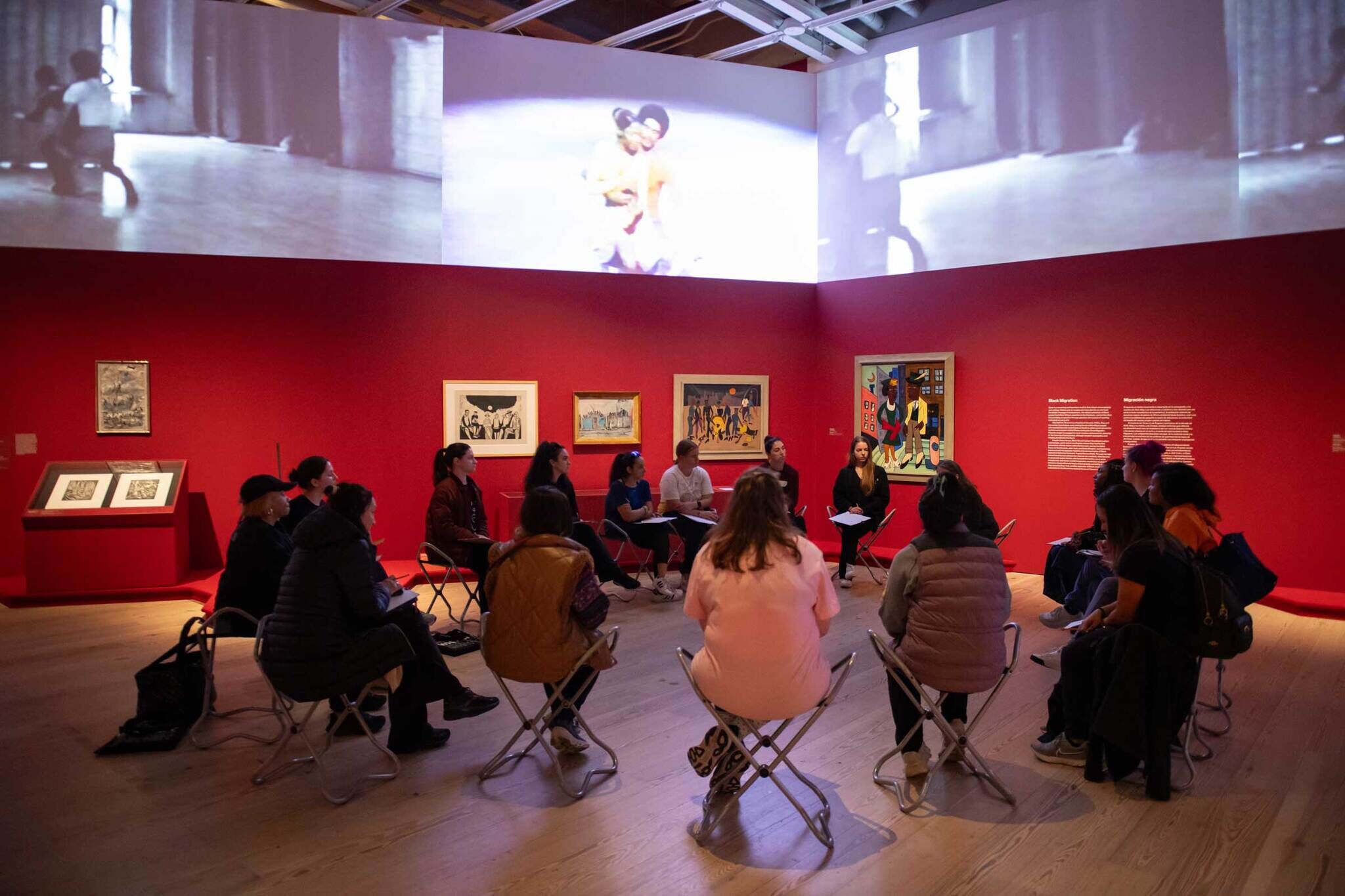 People sitting on stools in a gallery in a circle, engaging in dialogue. 