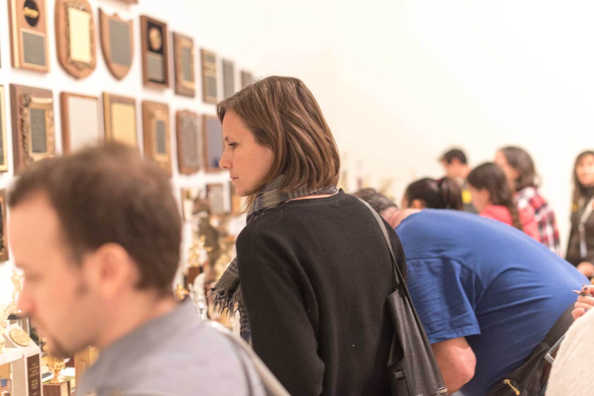 People looking at framed art on the wall. The frames are hung densely and made out of wood. 