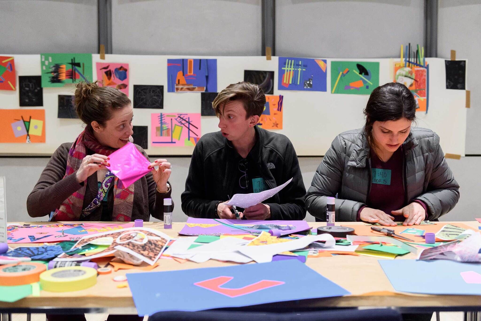 Three adults are engaging in an art-making activity, using colorful paper. 