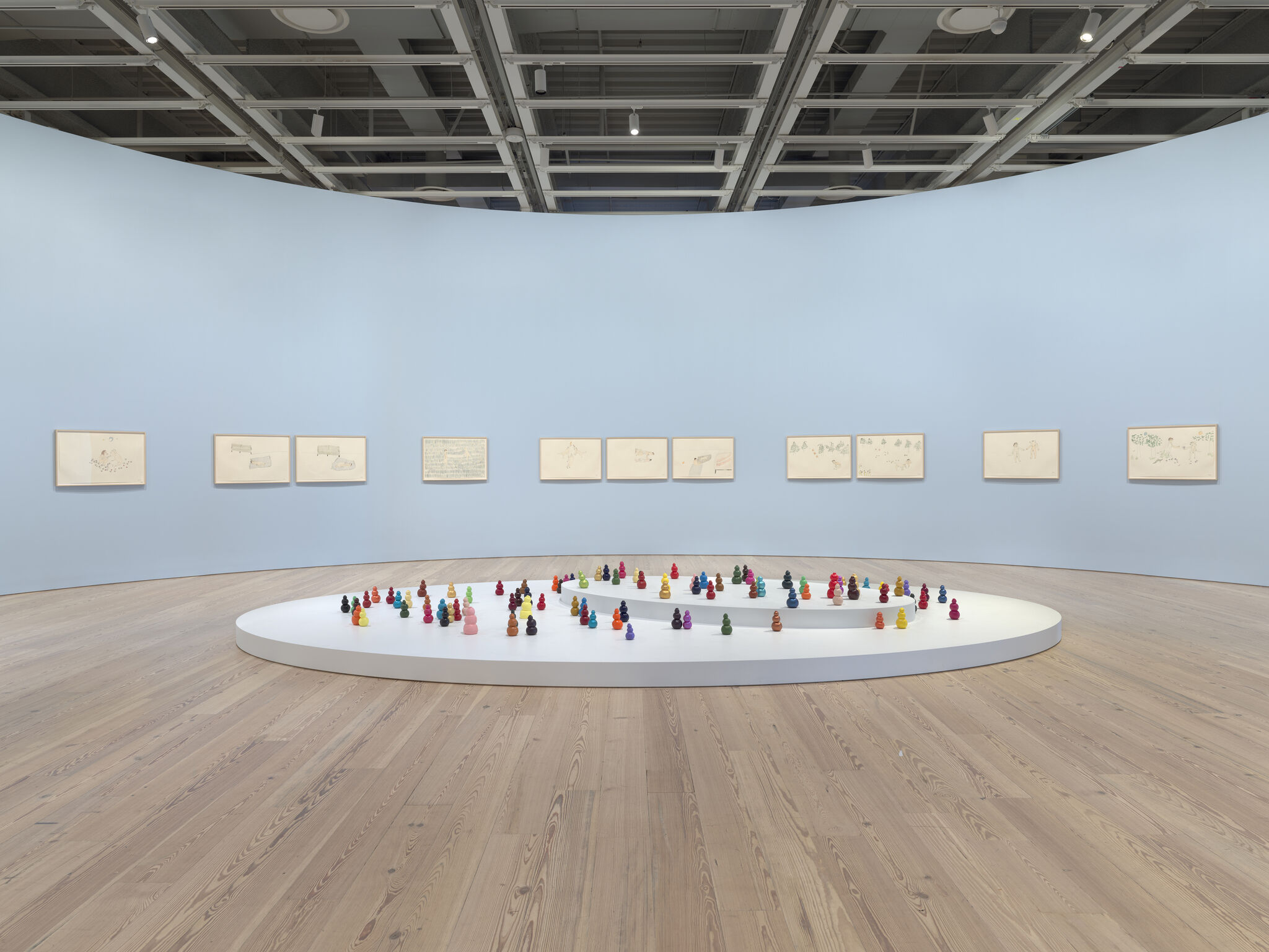 A curved gallery room features a circular platform with rows of small colorful figurines arranged in a spiral.