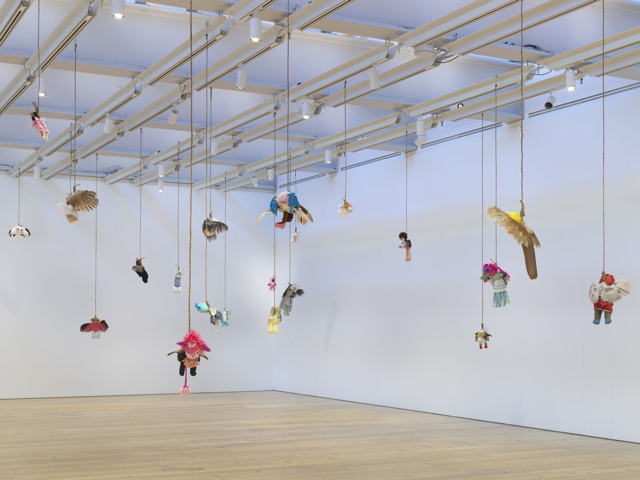 Several stuffed toys hang from ropes suspended from the ceiling in a brightly lit gallery.
