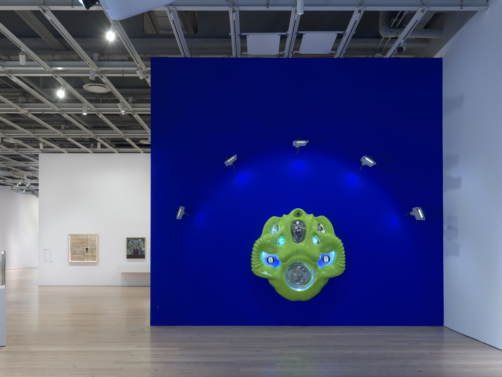 Bright green abstract wall sculpture lit by spotlights against a deep blue museum wall.