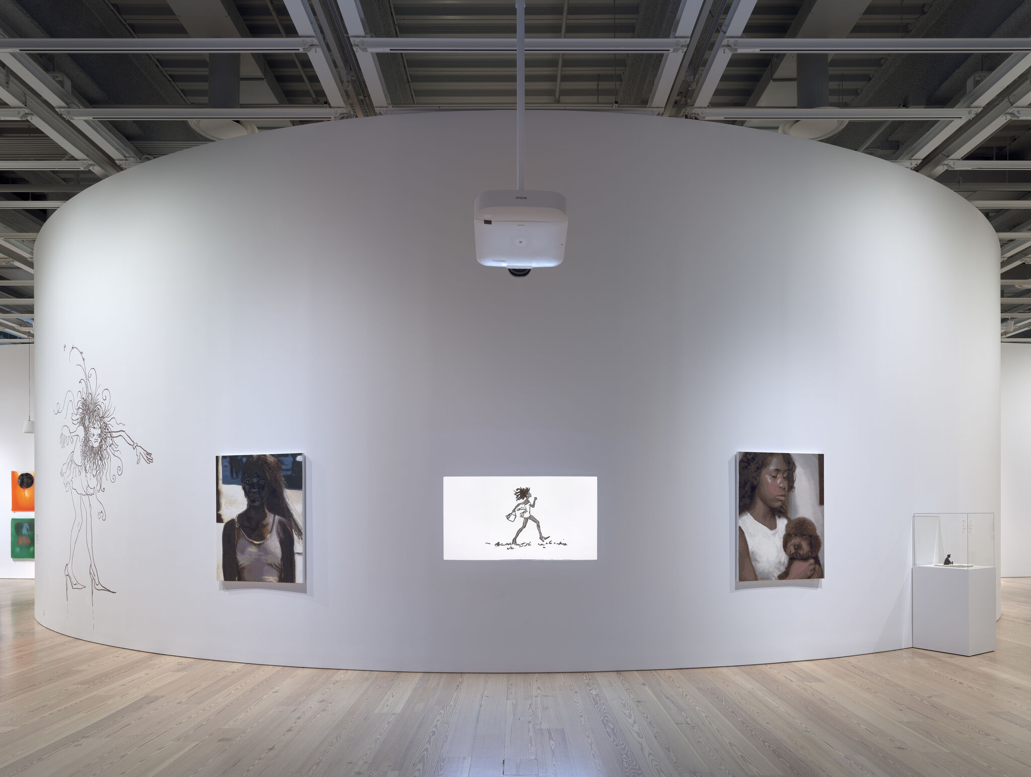 A curved white gallery wall displaying two portraits and a central projected walking figure under a ceiling projector.