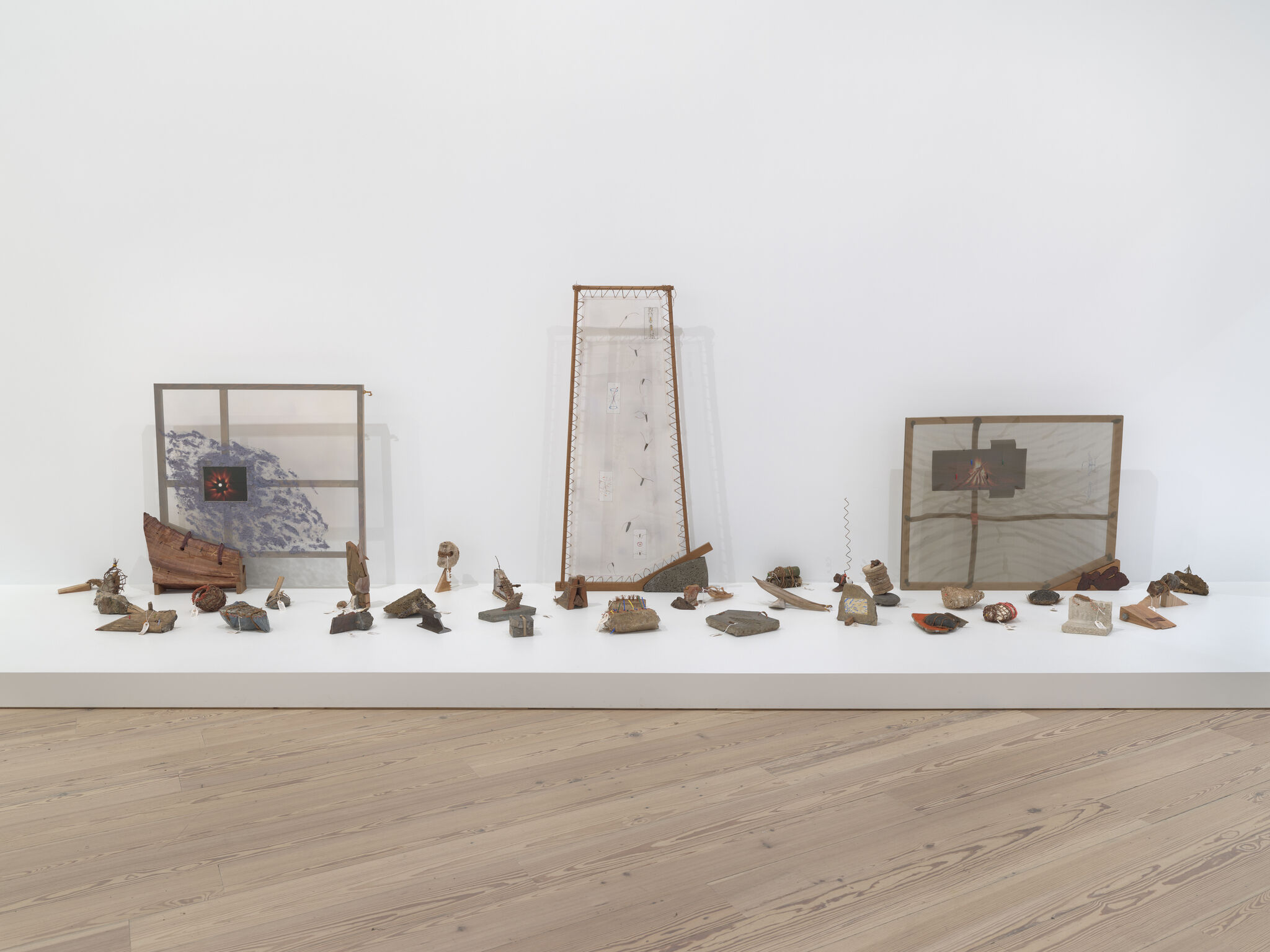 Small mixed-media sculptures and three translucent frames arranged in a long gallery display.