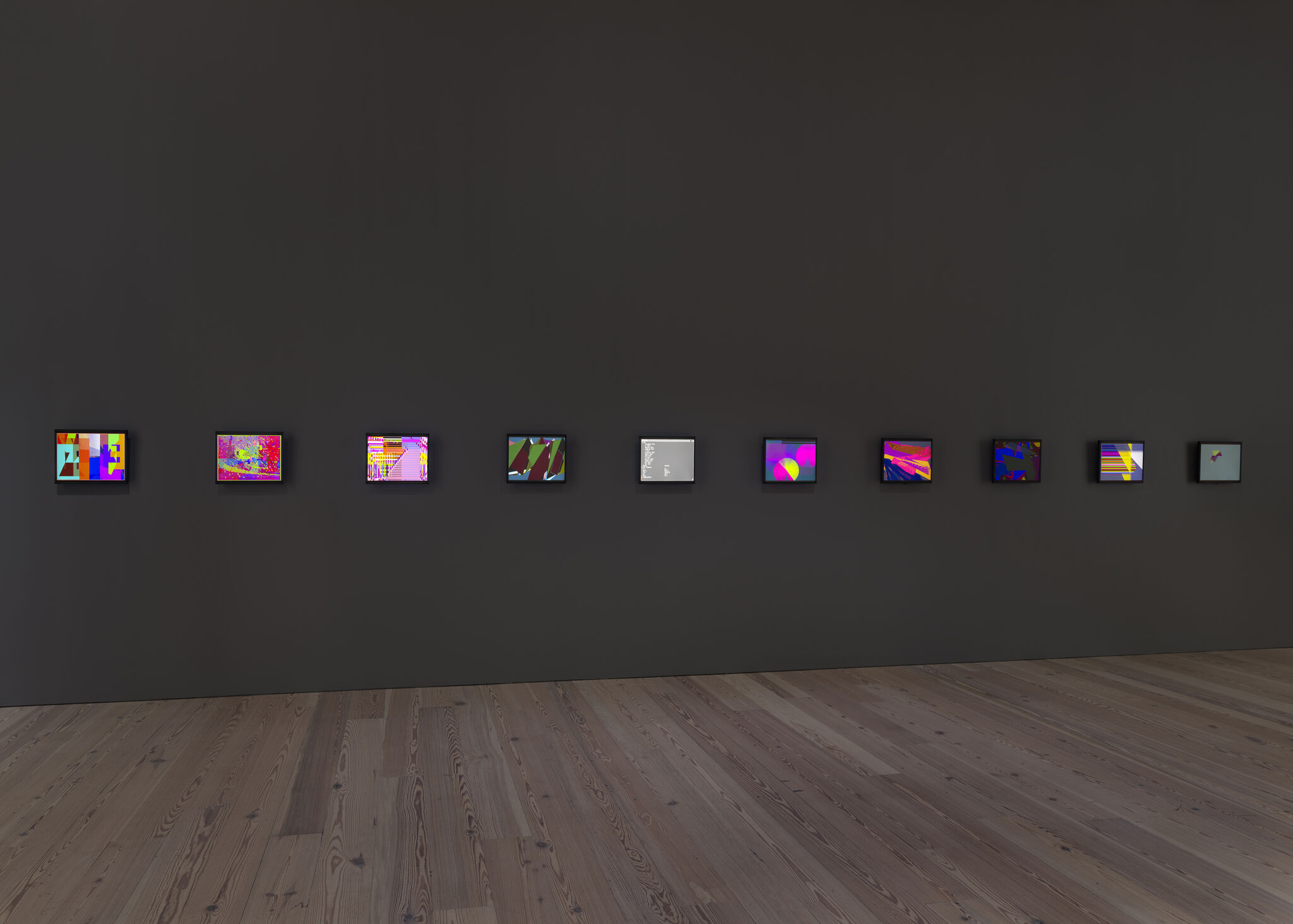 A row of small colorful digital artworks mounted evenly along a dark gallery wall.