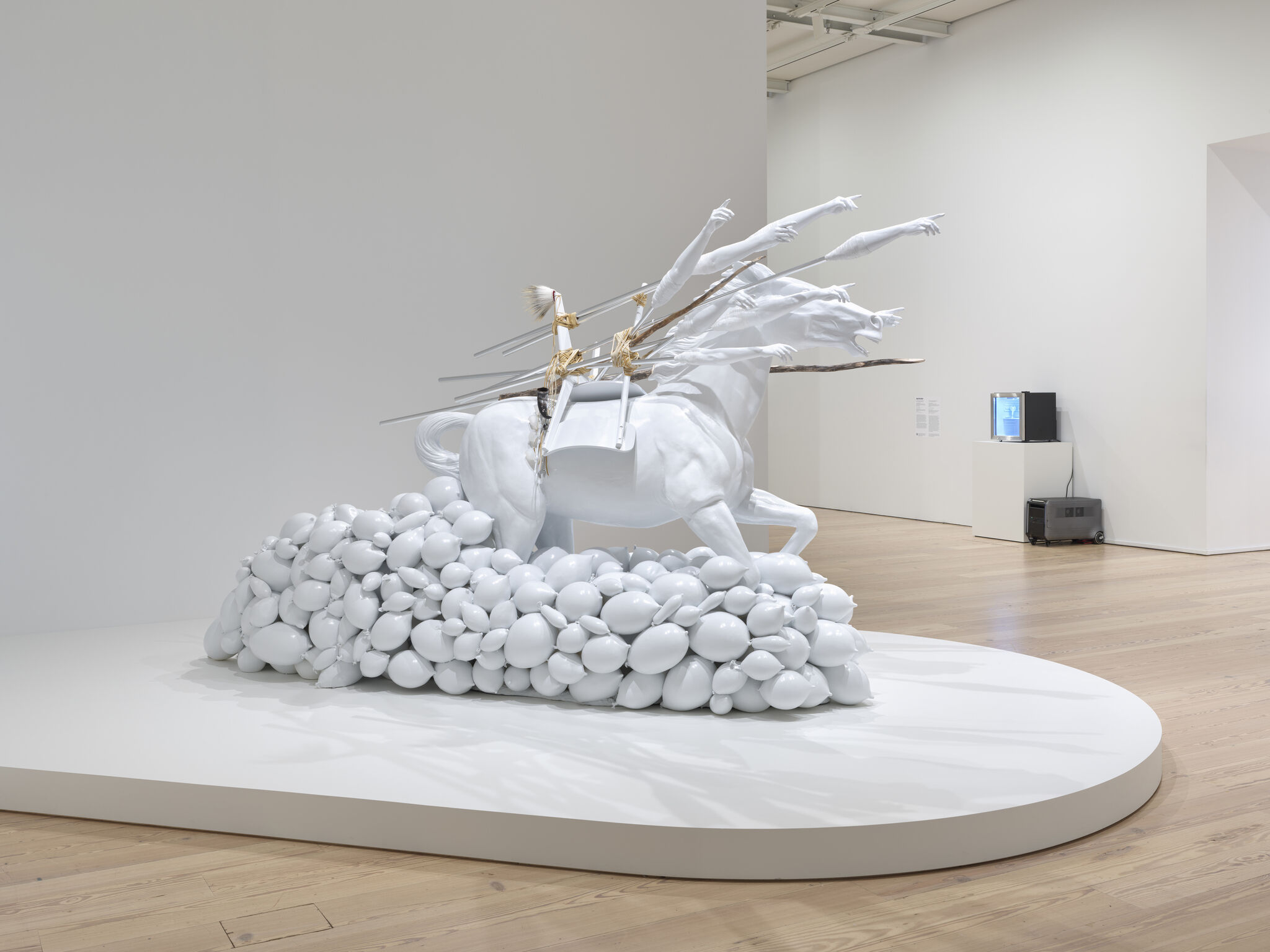 A white sculpture of a rearing horse with many outstretched arms and spears on a base of clustered balloon shapes.