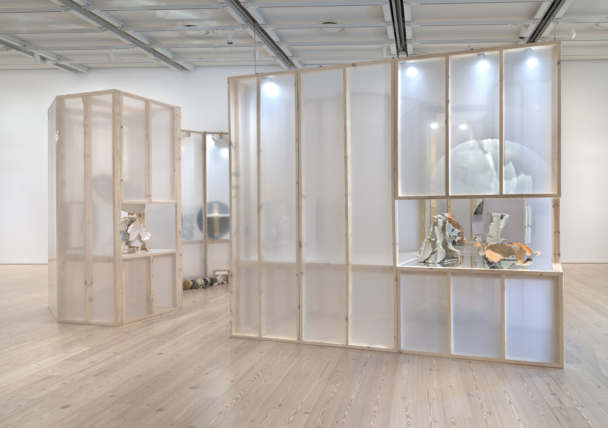 Translucent wooden partitions display abstract ceramic sculptures in a bright gallery space.