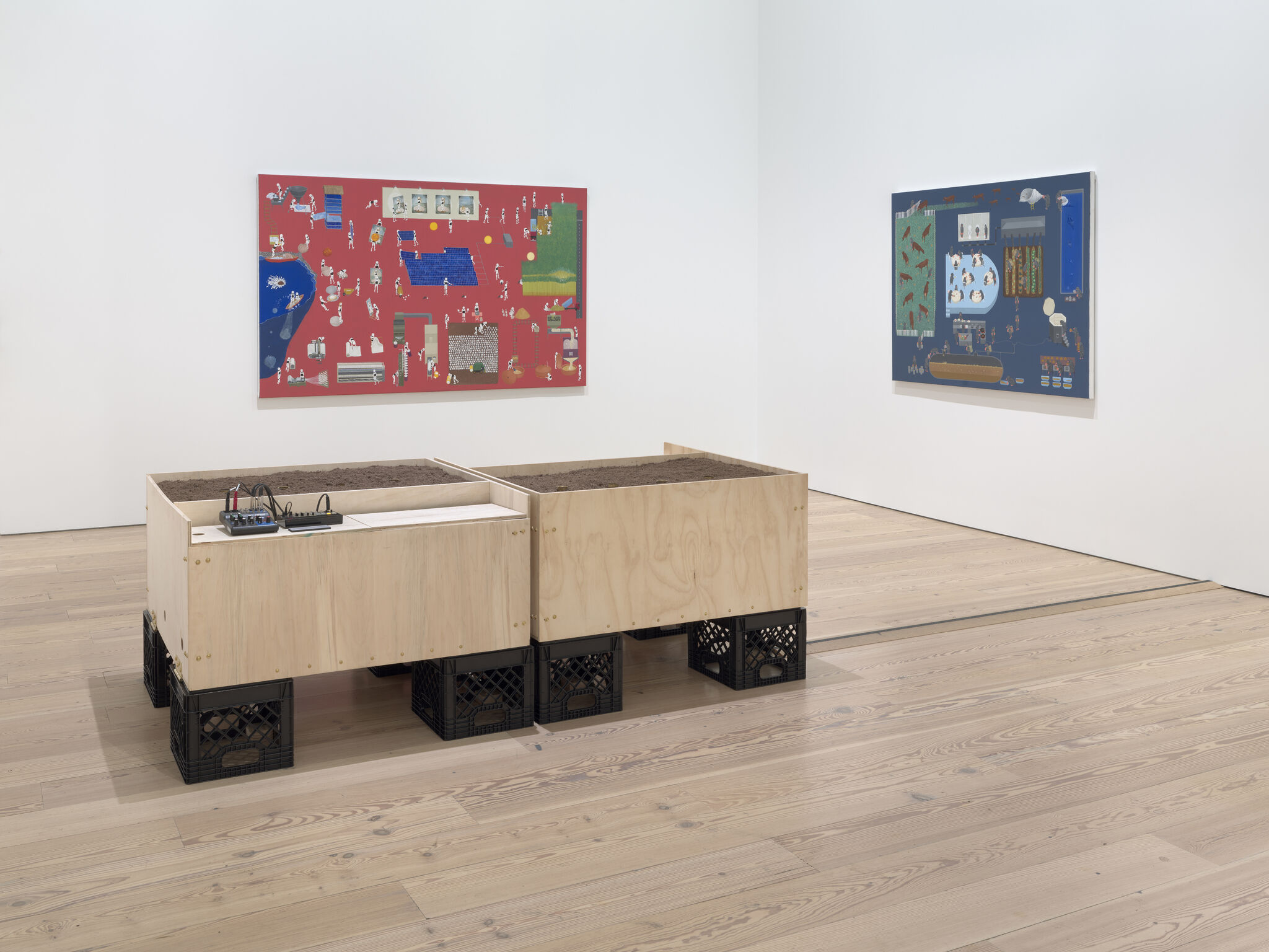 Three wooden planters filled with soil sit on black crates in a white gallery room.