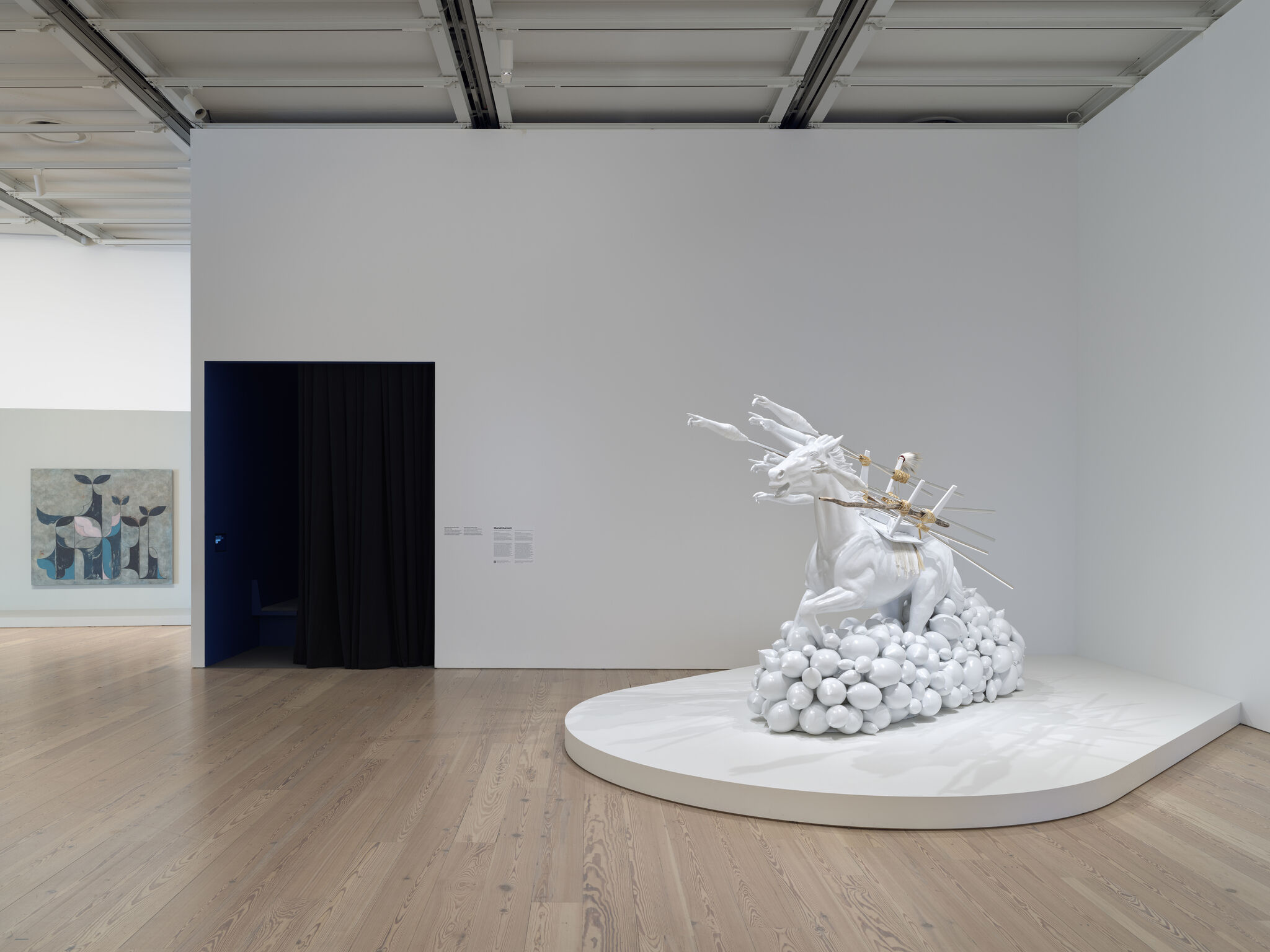 A glossy white sculpture of a rearing horse emerging from spherical clouds with figures pointing forward.