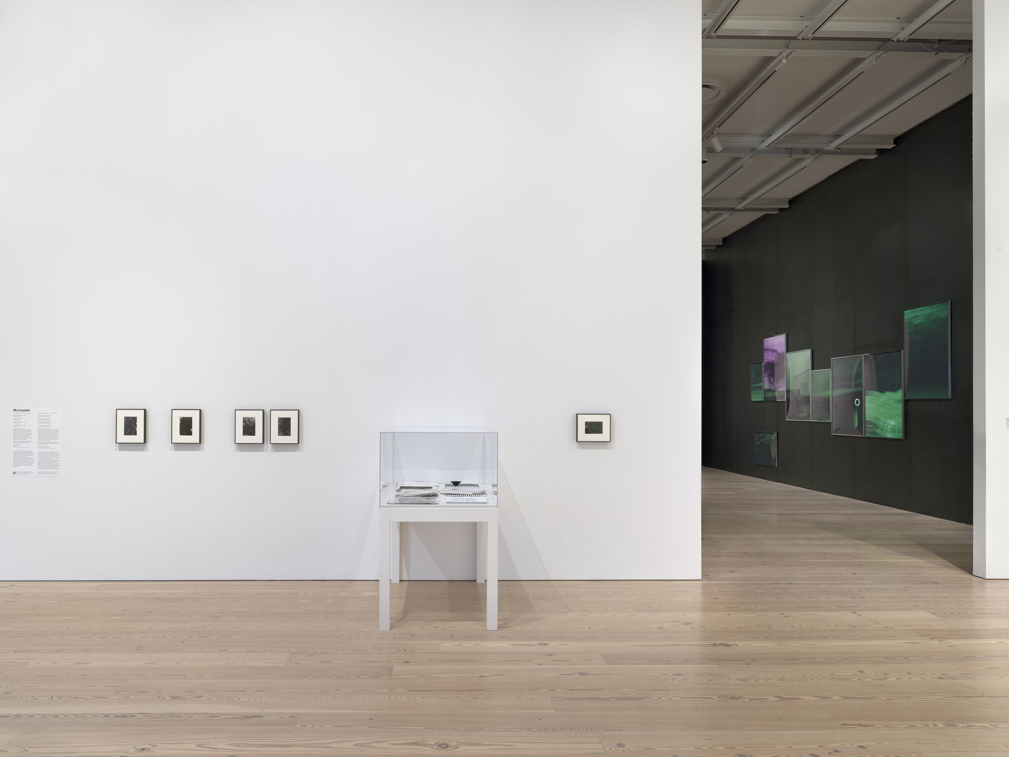 Minimal gallery wall with small framed photographs and a glass display case on a wooden floor.