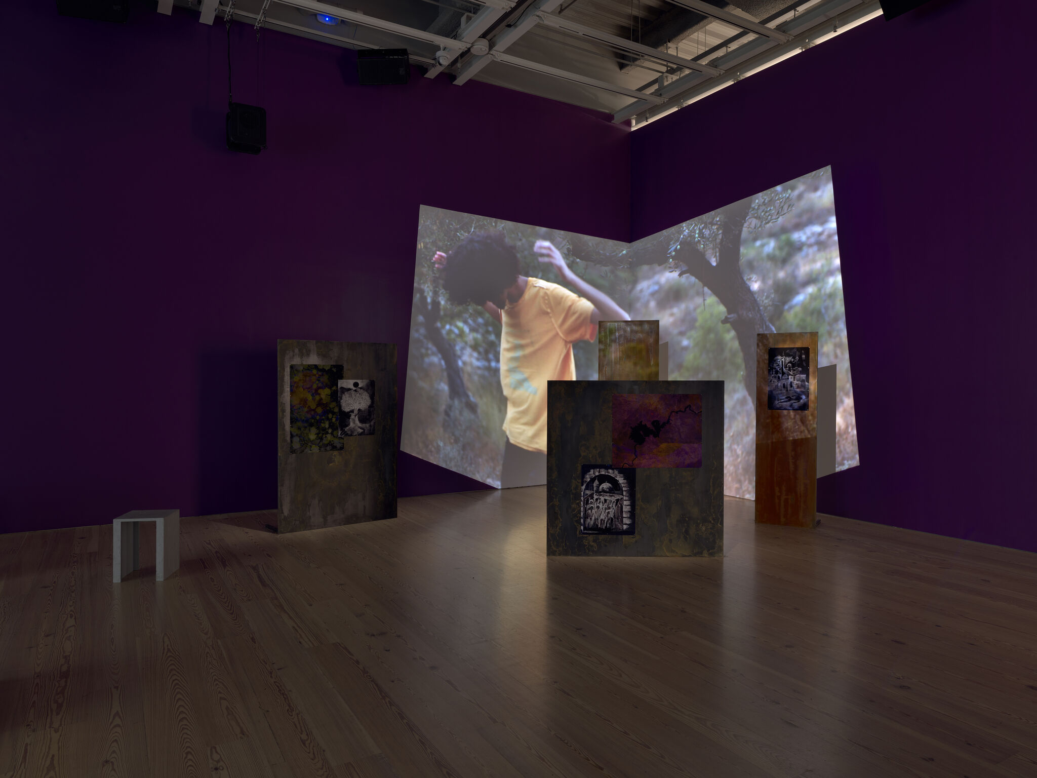 Gallery installation with a large video projection of a person in a yellow shirt and freestanding panels.