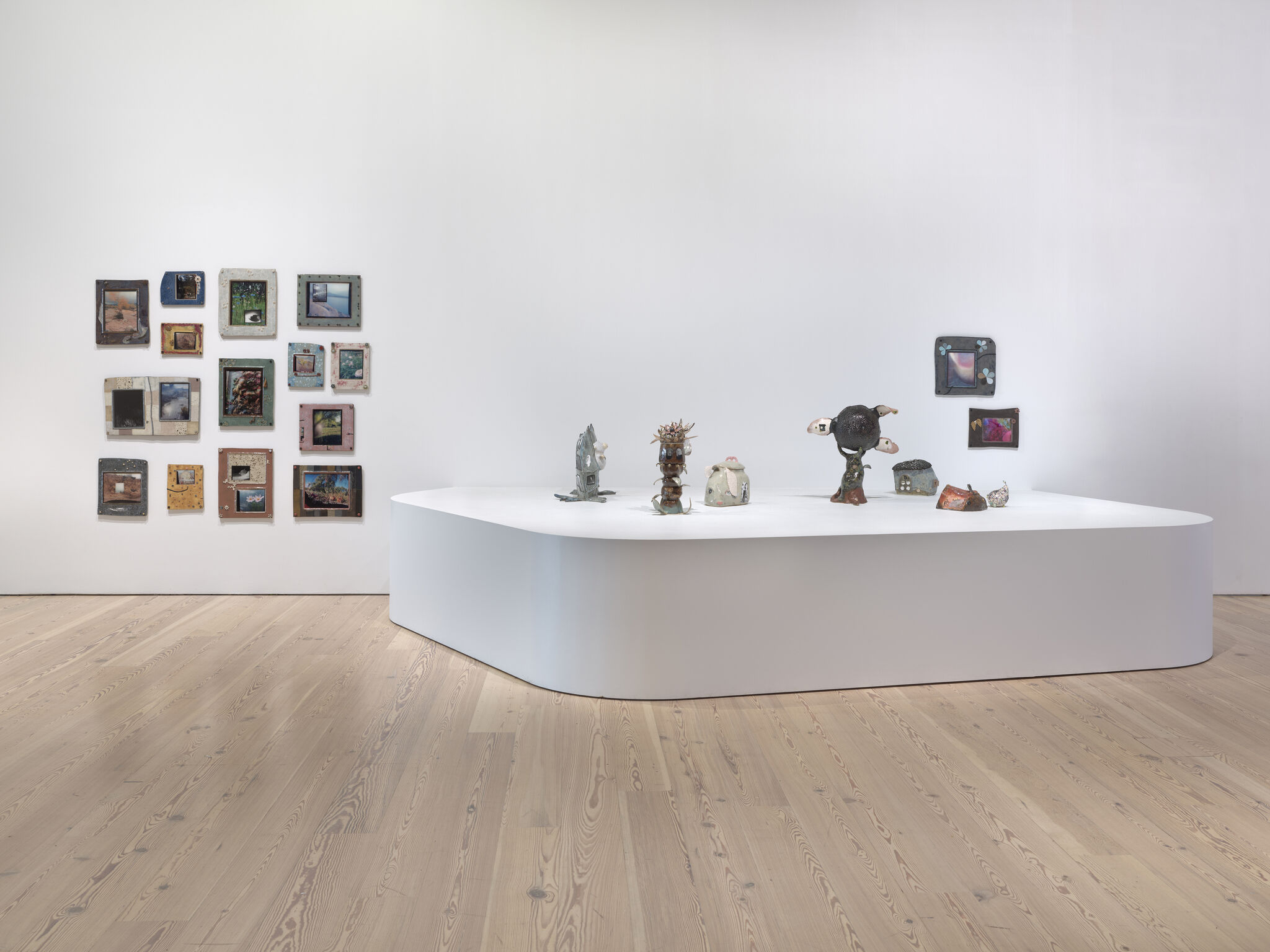 A platform displays small ceramic sculptures with a grid of colorful framed artworks on the wall.
