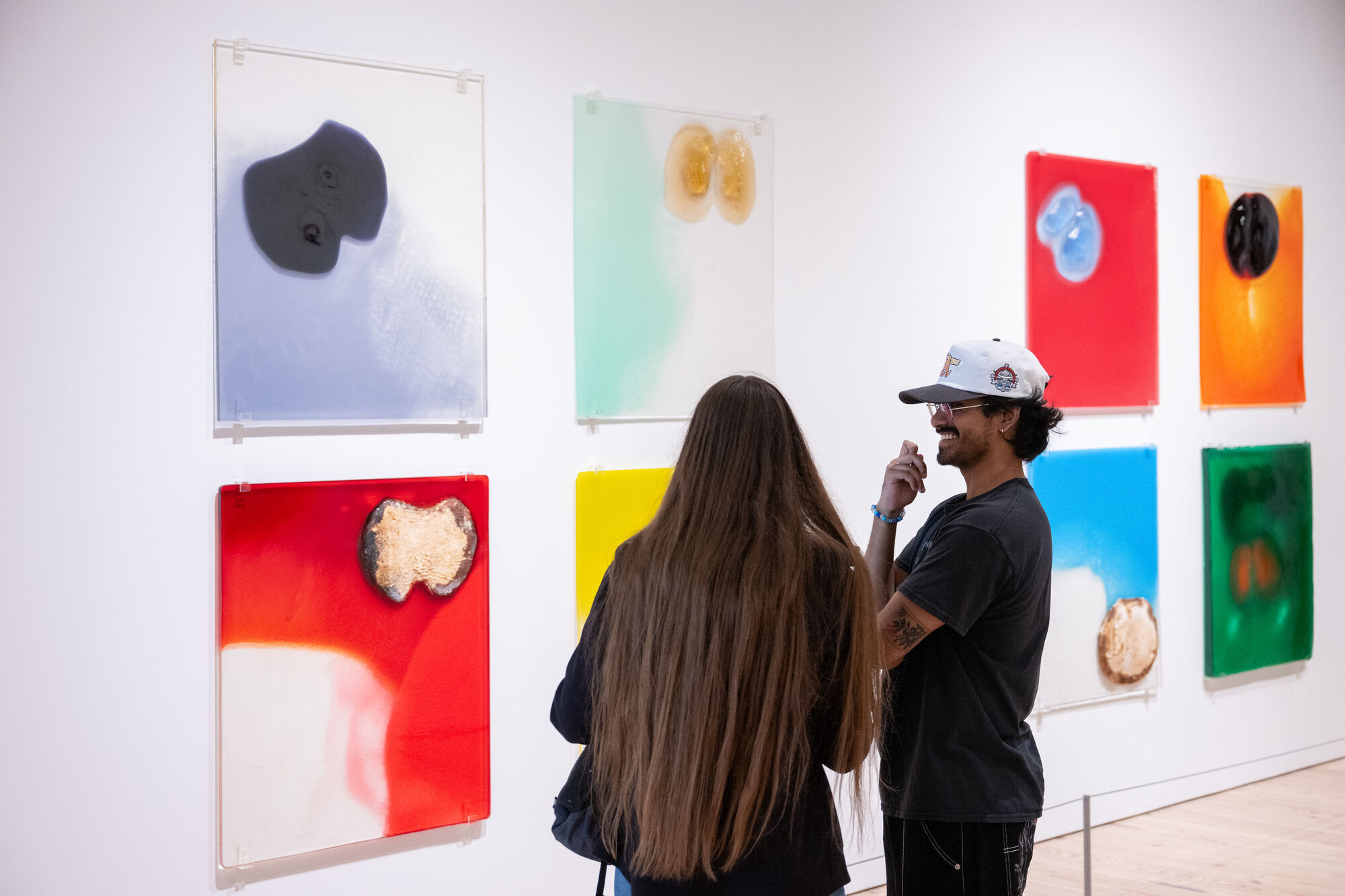 A smiling man and a woman look and talk while viewing colorful abstract panels on the wall.