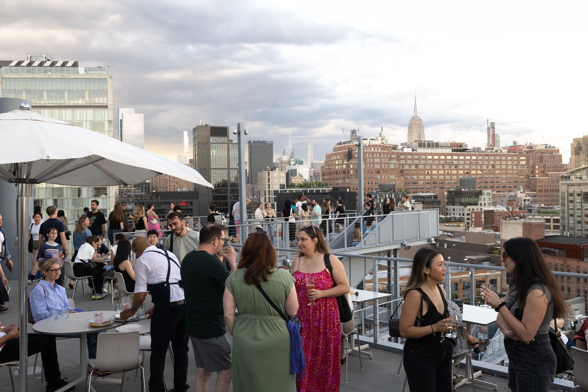A crowded rooftop terrace with people socializing and drinking against a city skyline.