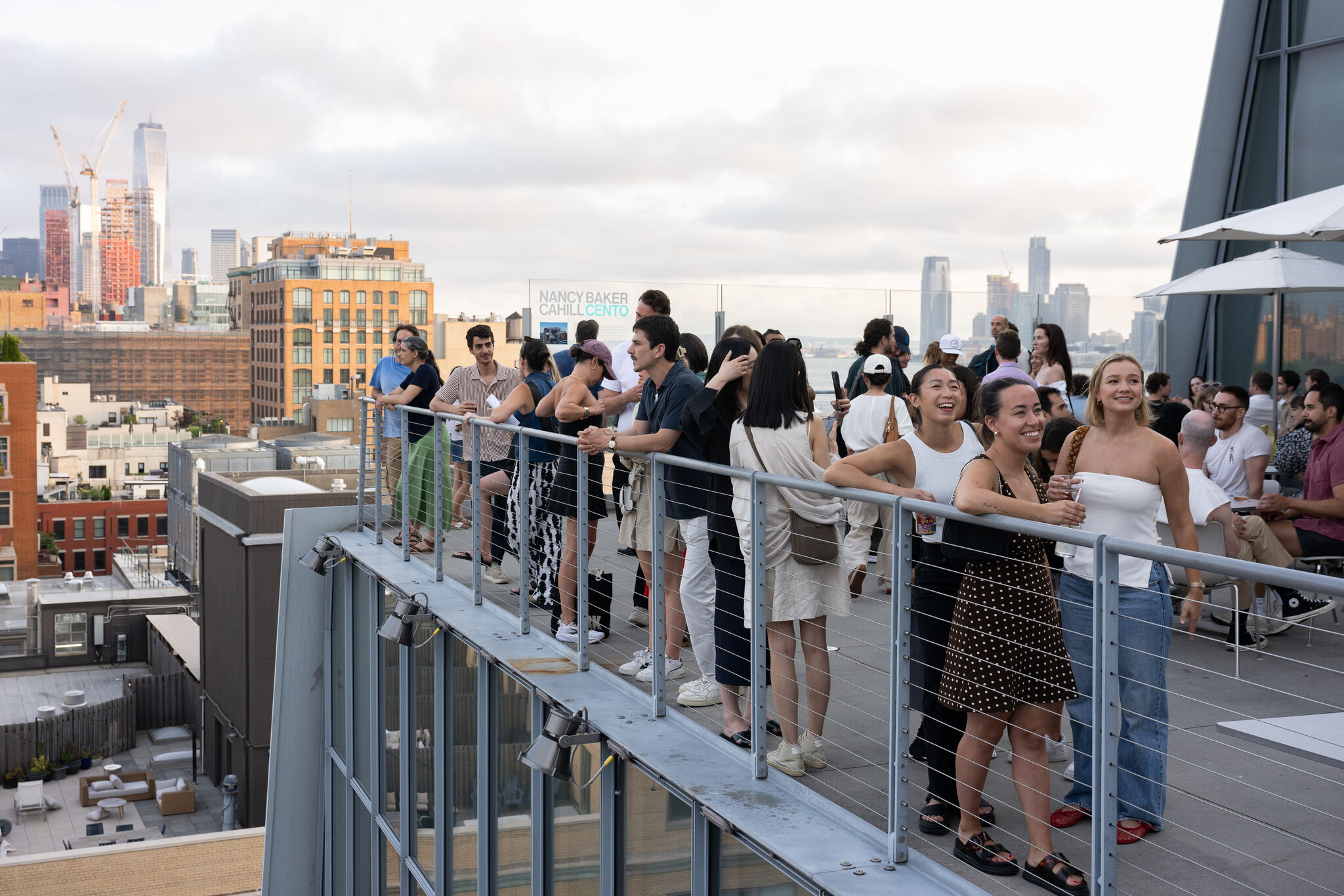 A diverse group of people socialize and enjoy skyline views on a crowded rooftop terrace.