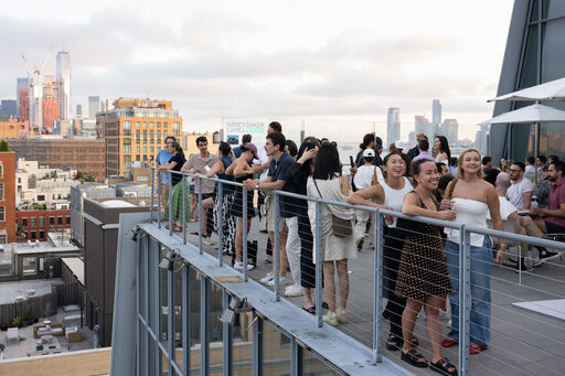 A diverse group of people socialize and enjoy skyline views on a crowded rooftop terrace.