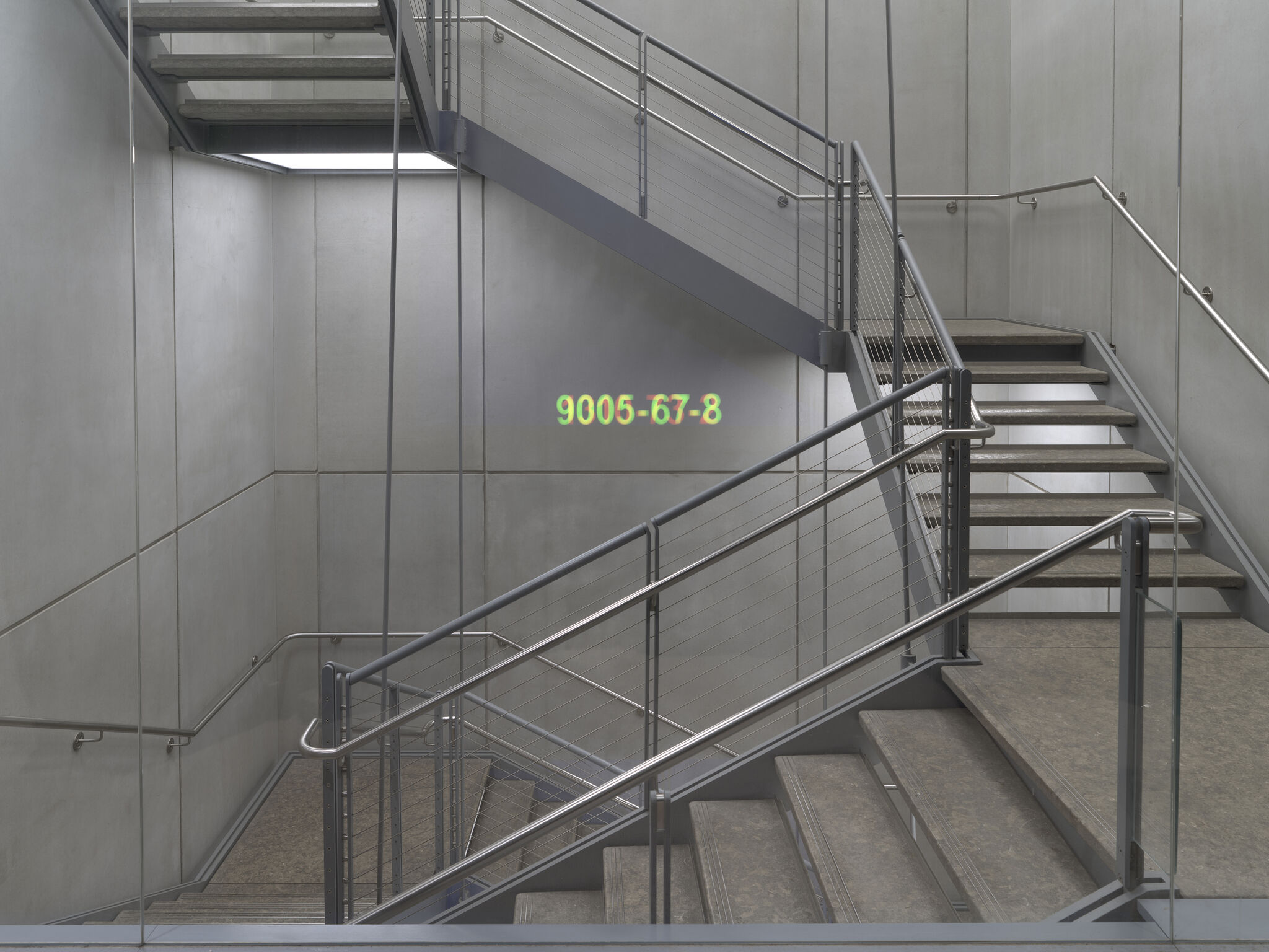 A steel and concrete stairwell with metal railings and a colorful code projected on the wall.