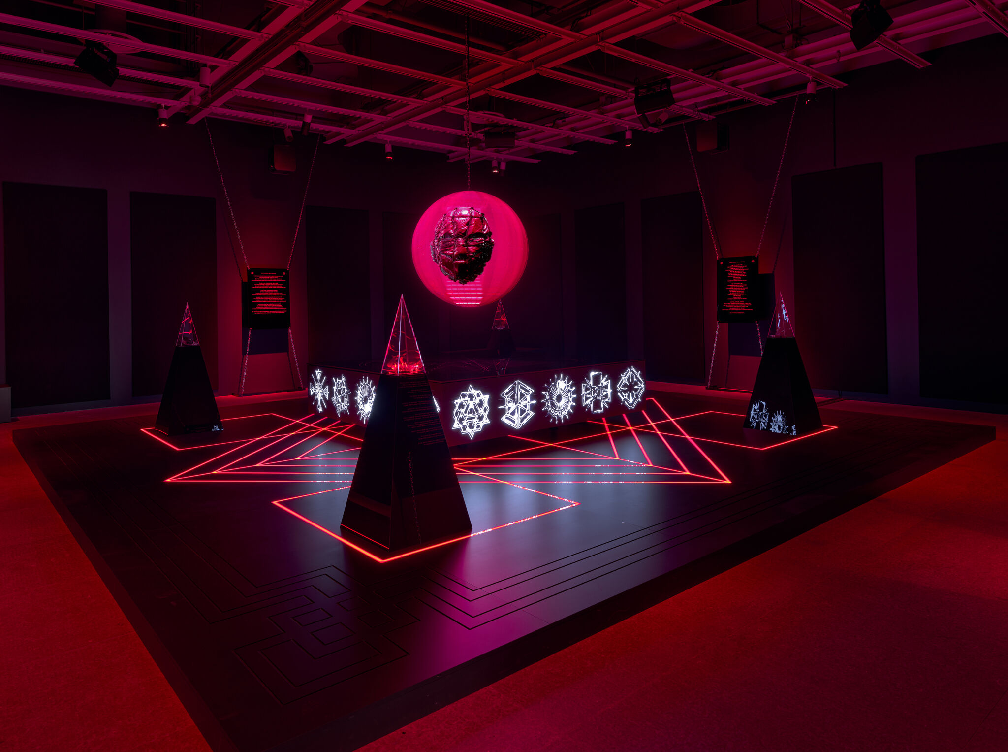 A glowing pink orb with suspended sculpted head hovers above a neon-lit geometric display.