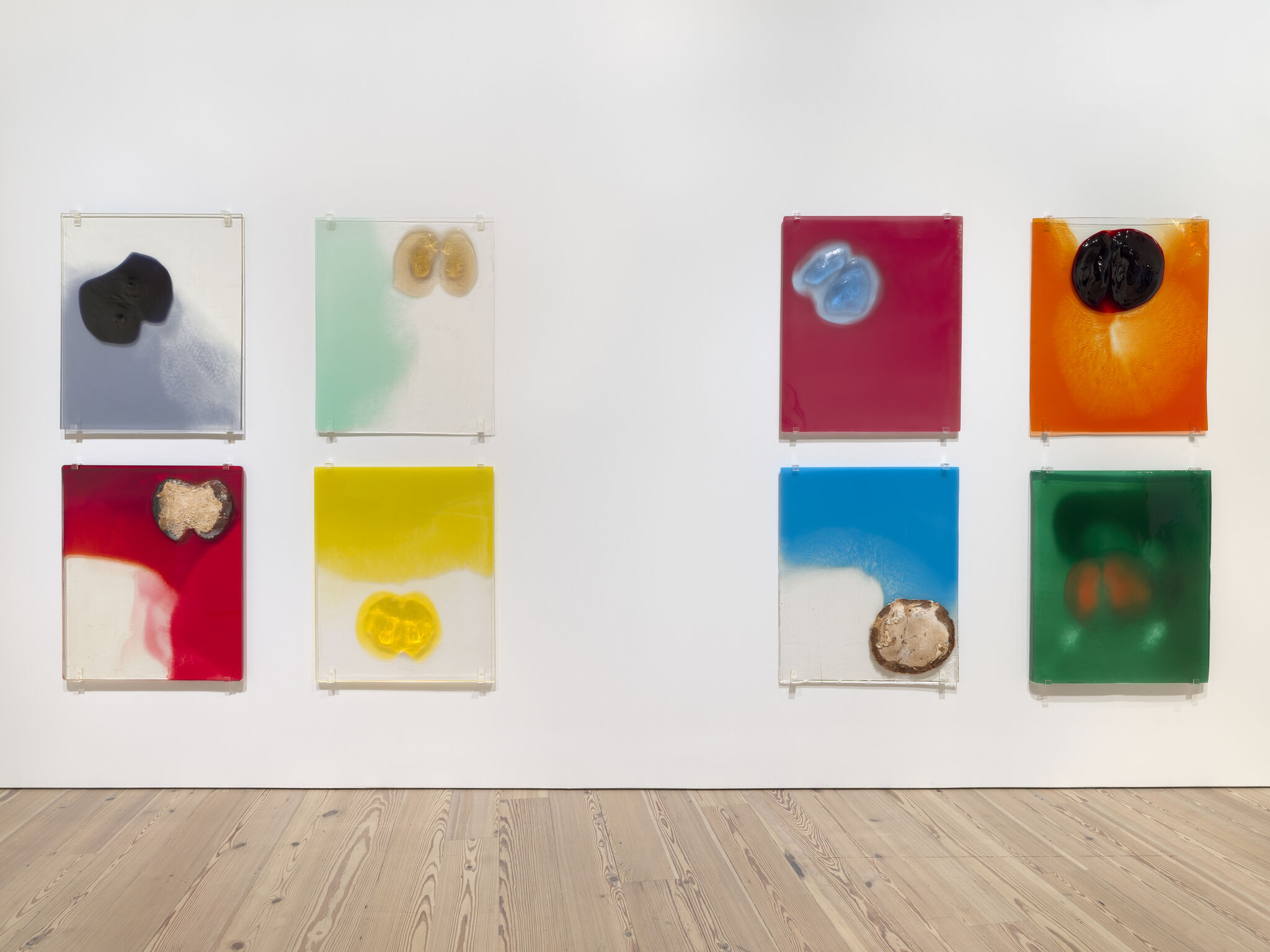 Eight pieces of big "slides" of various bright colors with various splotches on a white wall.
