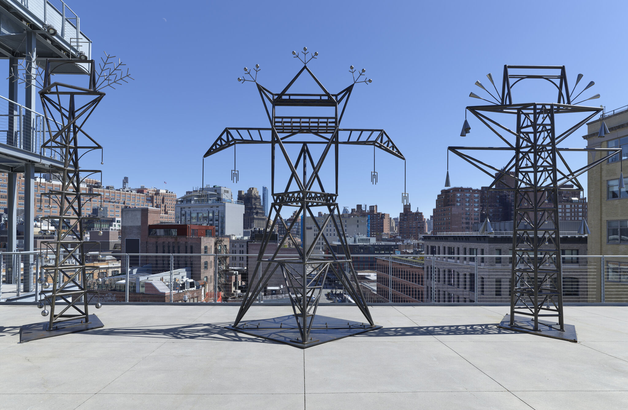 On a terrace overlooking a busy cityscape, three utility pole-like sculptures stand. They have extra additional decorations as well.